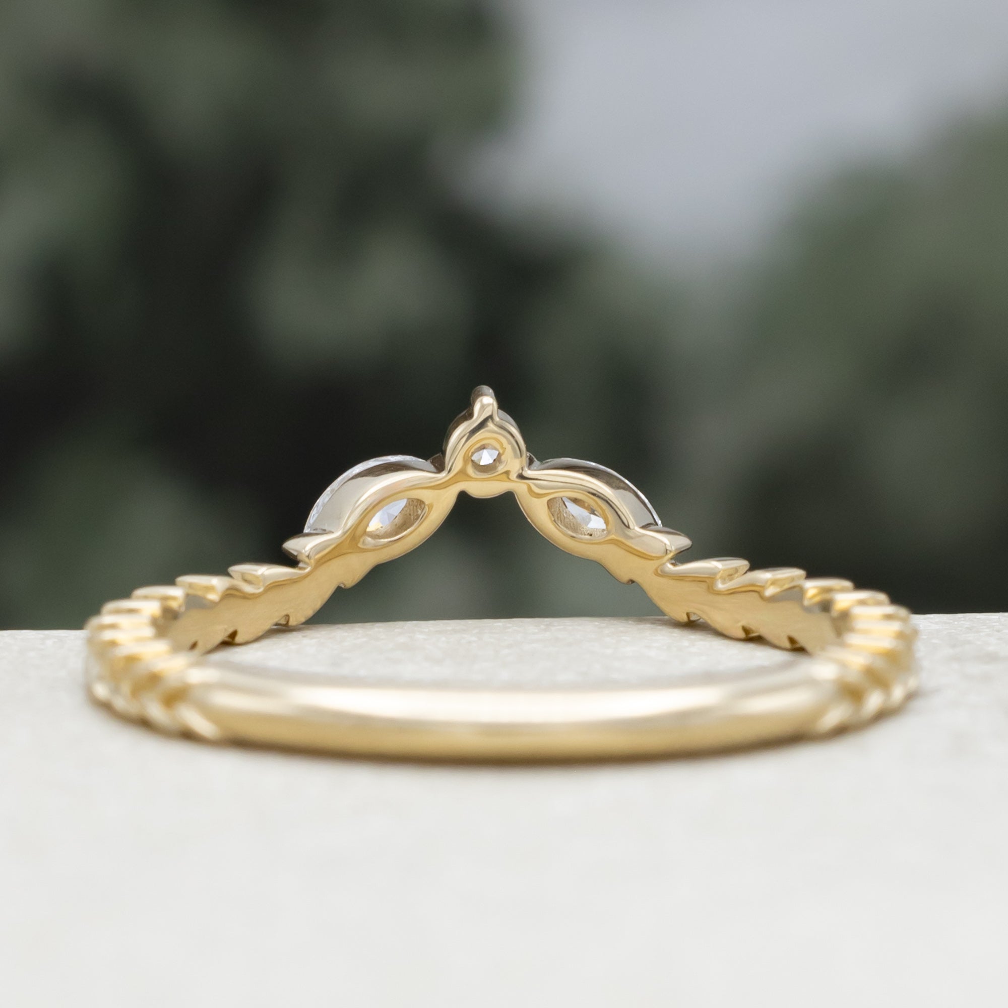 A yellow gold ring tracer with three diamond accents on a vine style band against a blurred green background