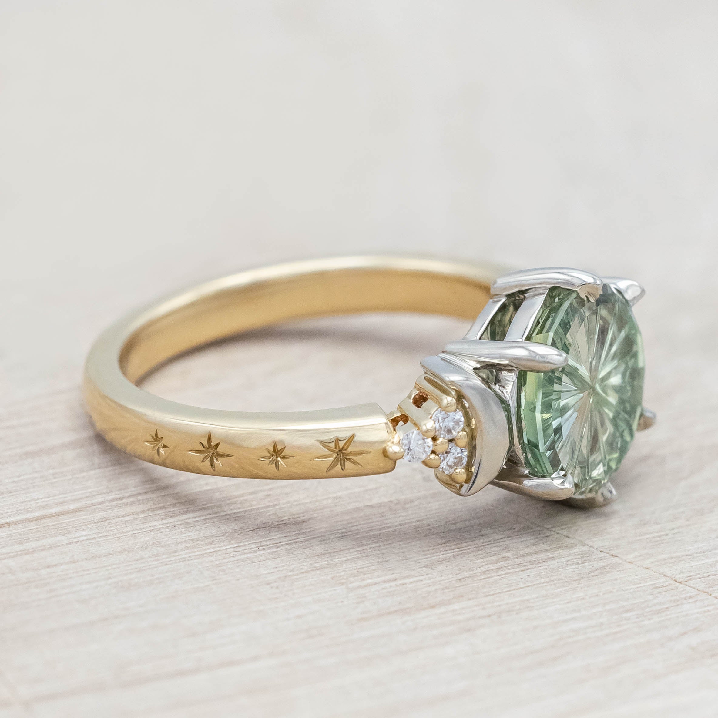 Gold ring with a green sapphire and crescent moon accents on a light wooden surface