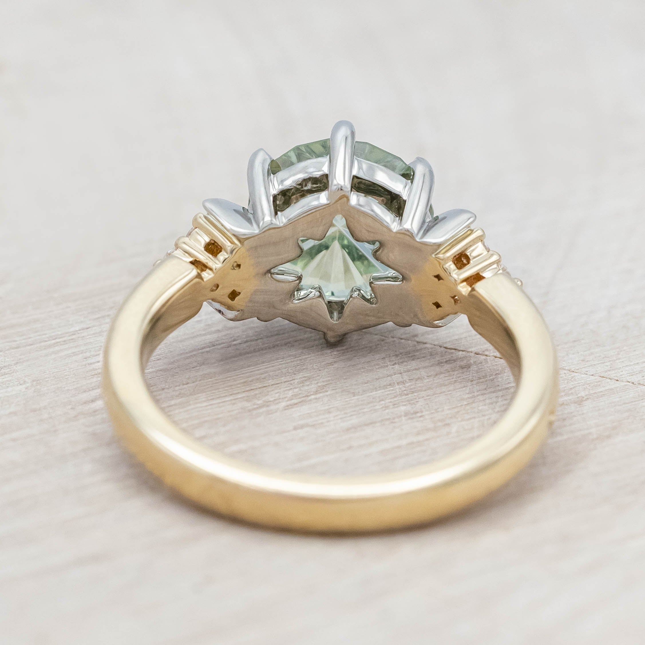 Gold ring with a green sapphire and crescent moon accents on a light wooden surface