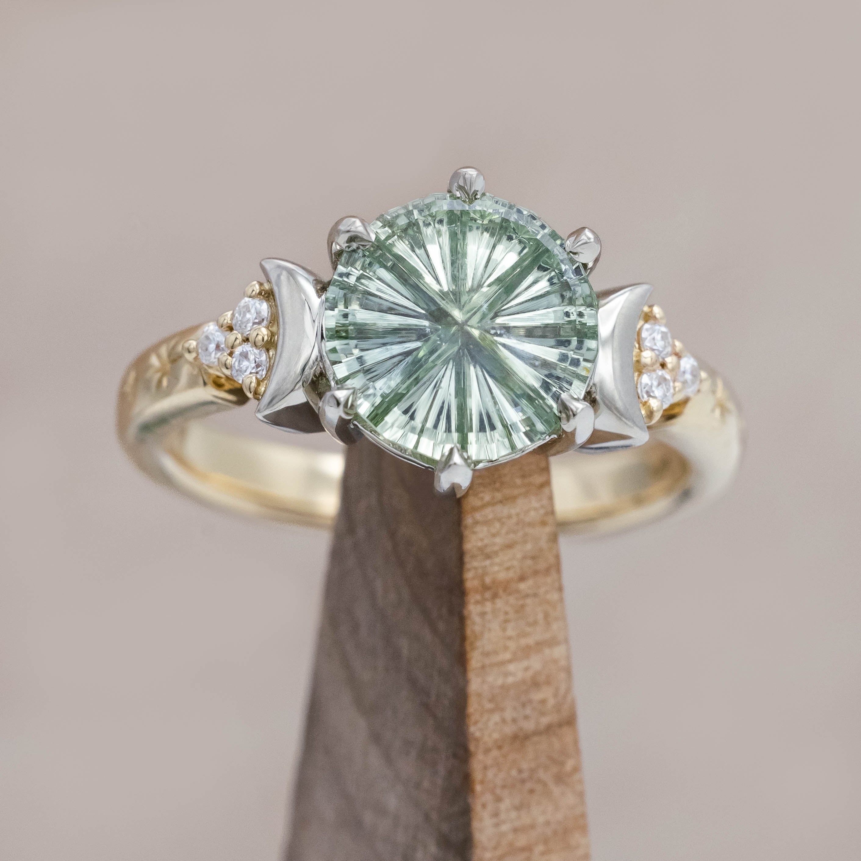 Gold ring with a green sapphire and crescent moon accents on a wooden stand against a beige background