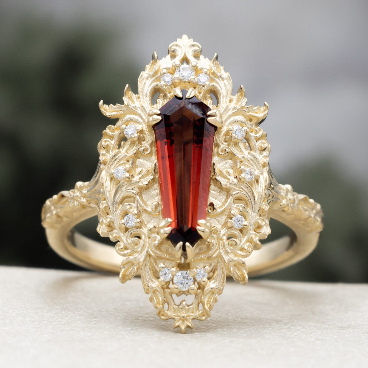 A gold ring with dagger cut garnet and diamond accents against a blured green background