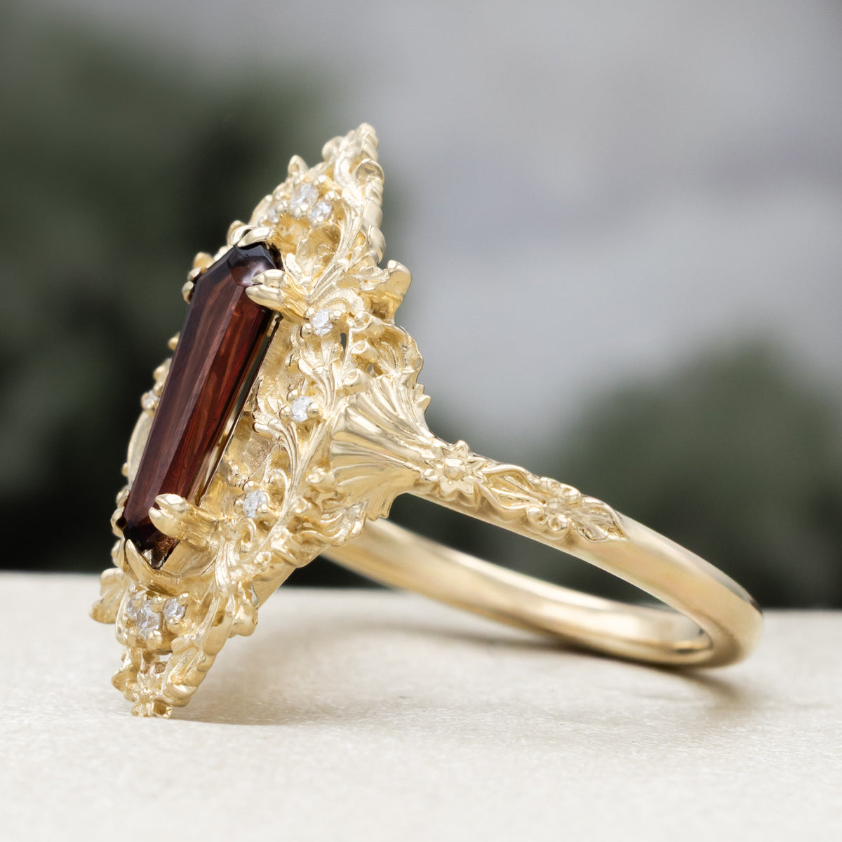 A gold ring with dagger cut garnet and diamond accents against a blured green background