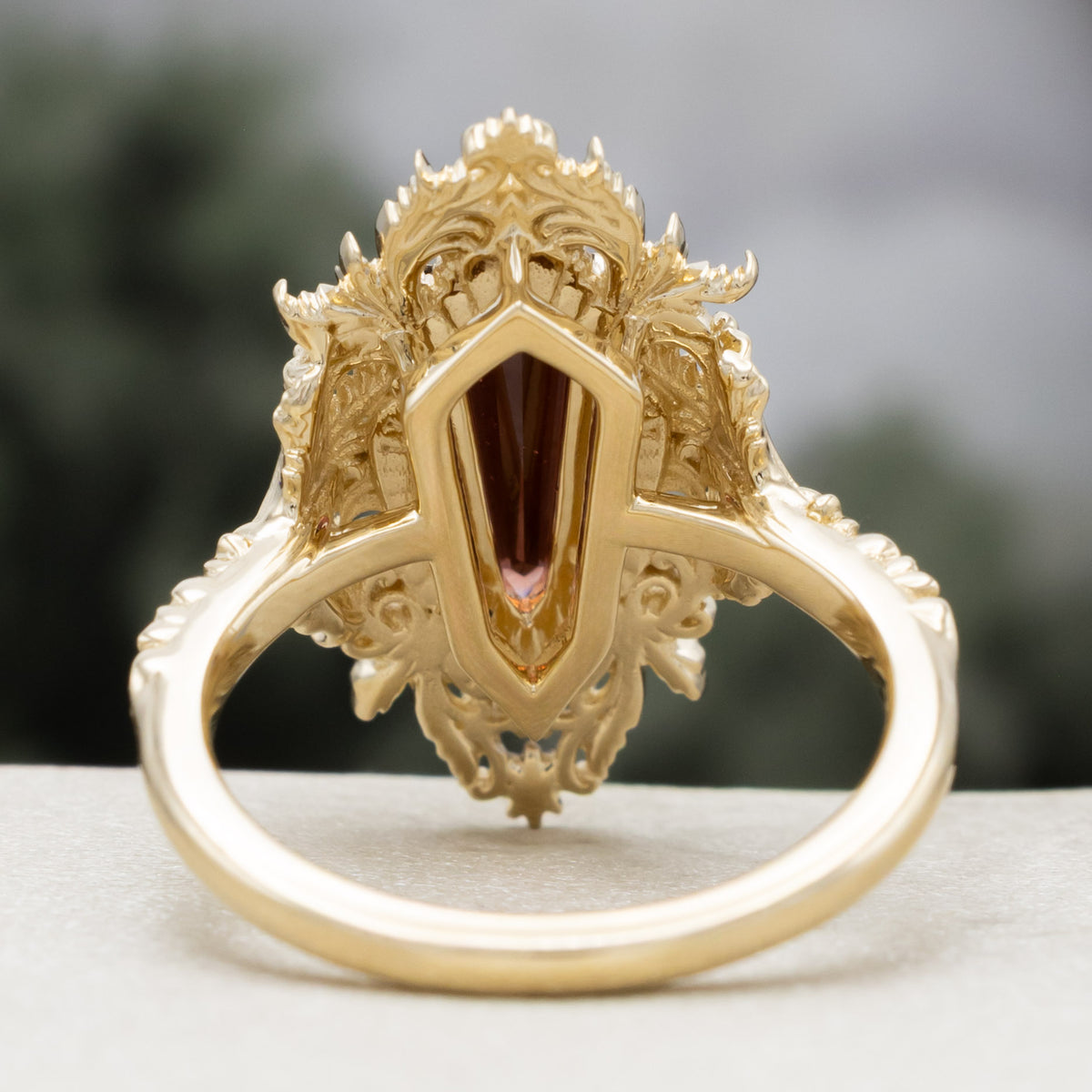 A gold ring with dagger cut garnet and diamond accents against a blured green background