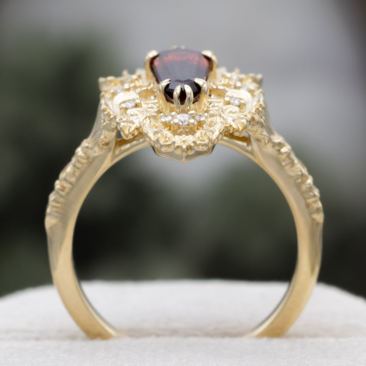 A gold ring with dagger cut garnet and diamond accents against a blured green background