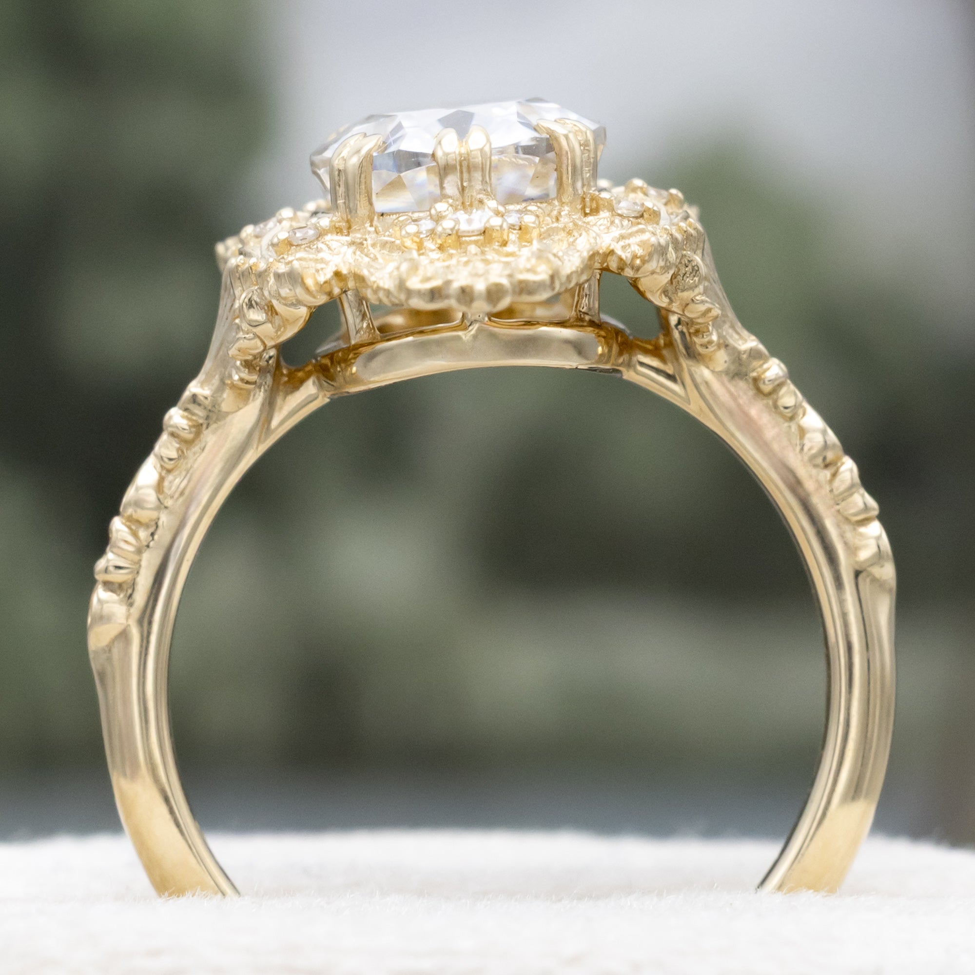 Gold ring with a large moissanite and intricate filigree on a neutral background