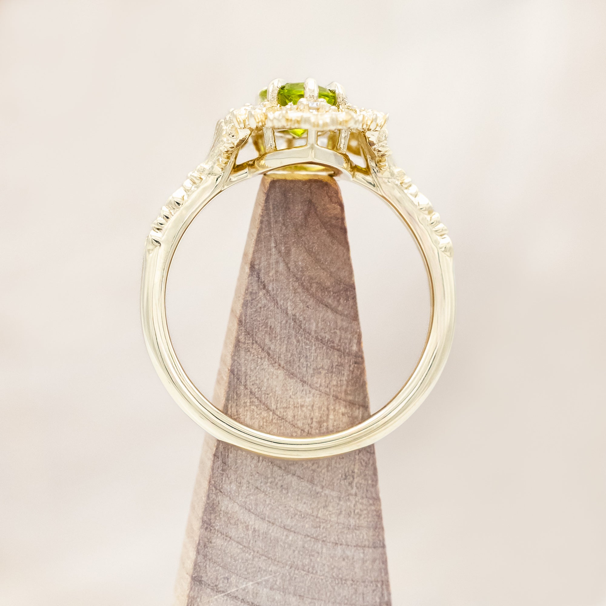 Yellow gold ring with a green peridot on a beige background