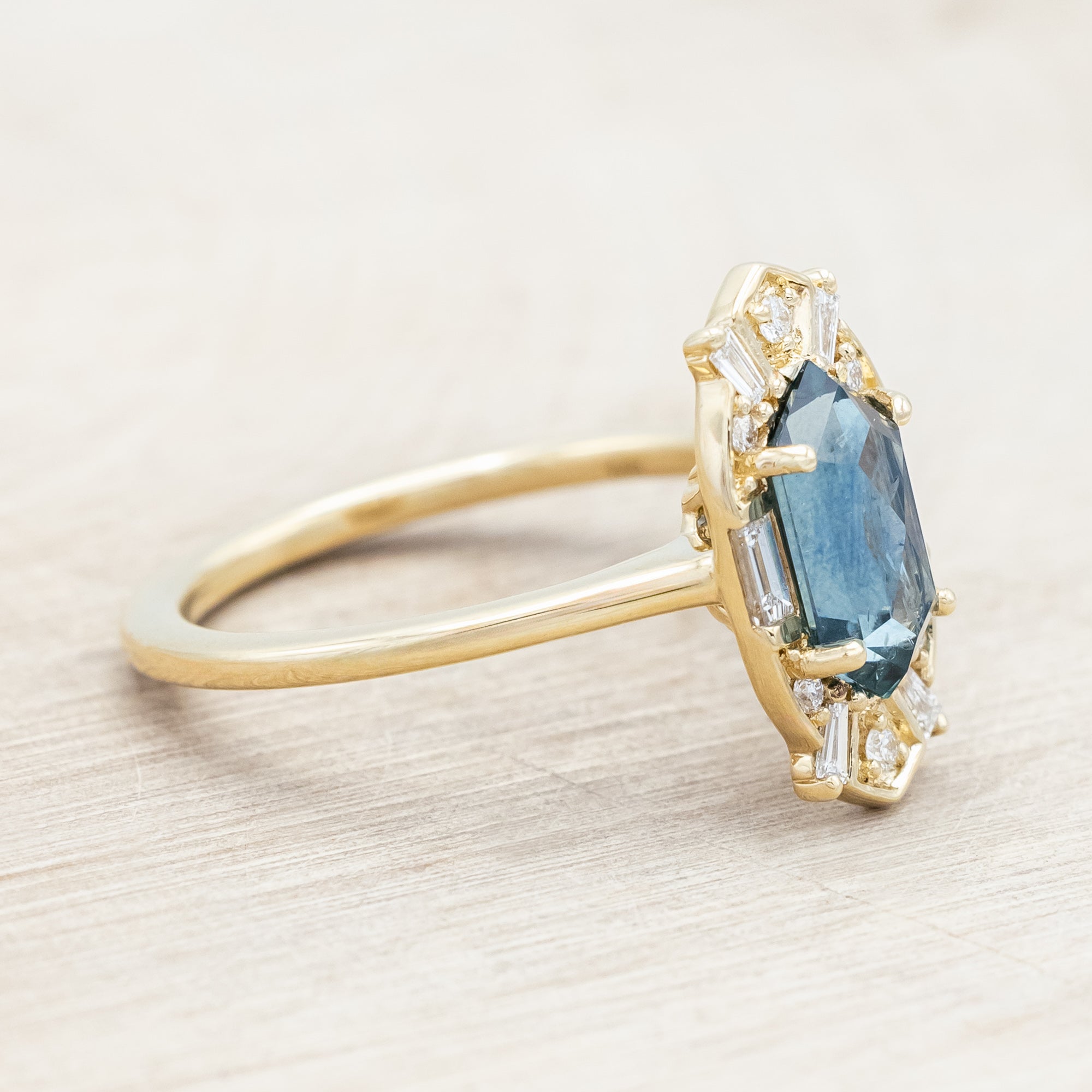 14K gold ring with Montana sapphire and diamond accents on a beige background