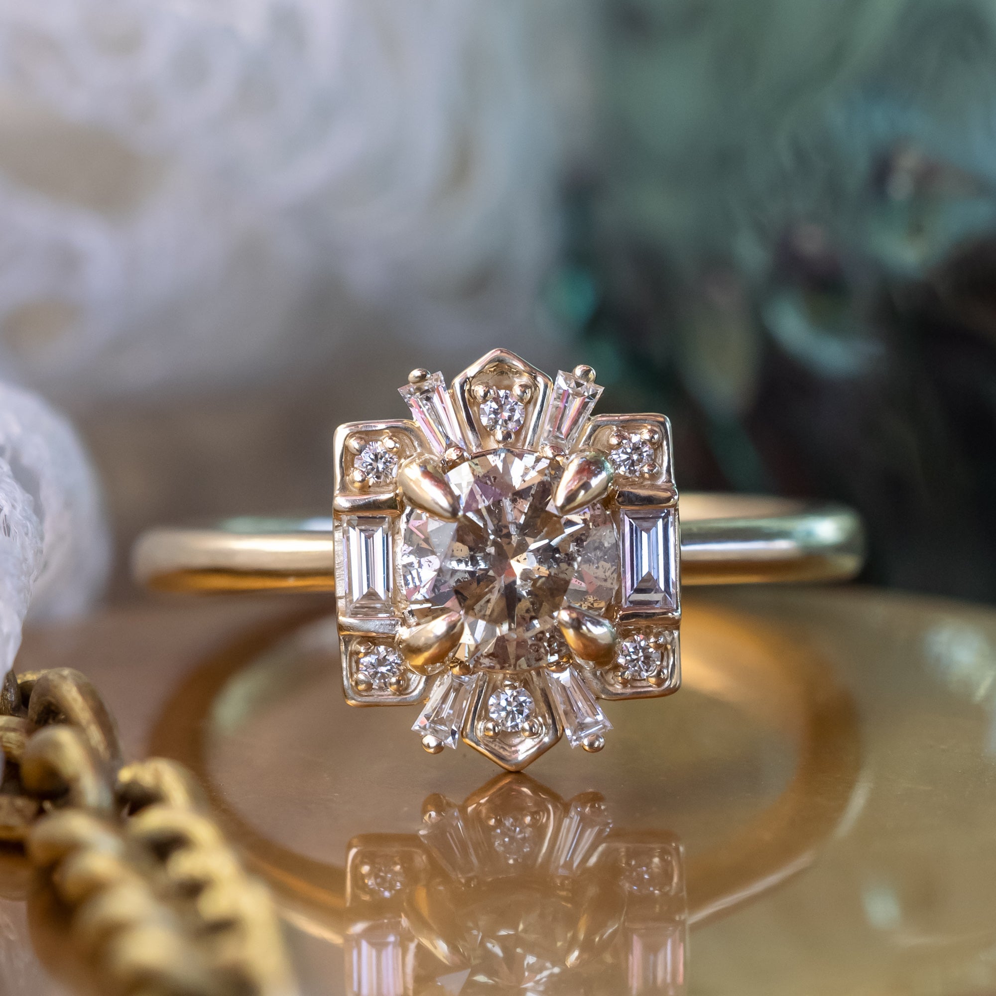 Gold ring with champagne diamond and diamond halo on a reflective surface.