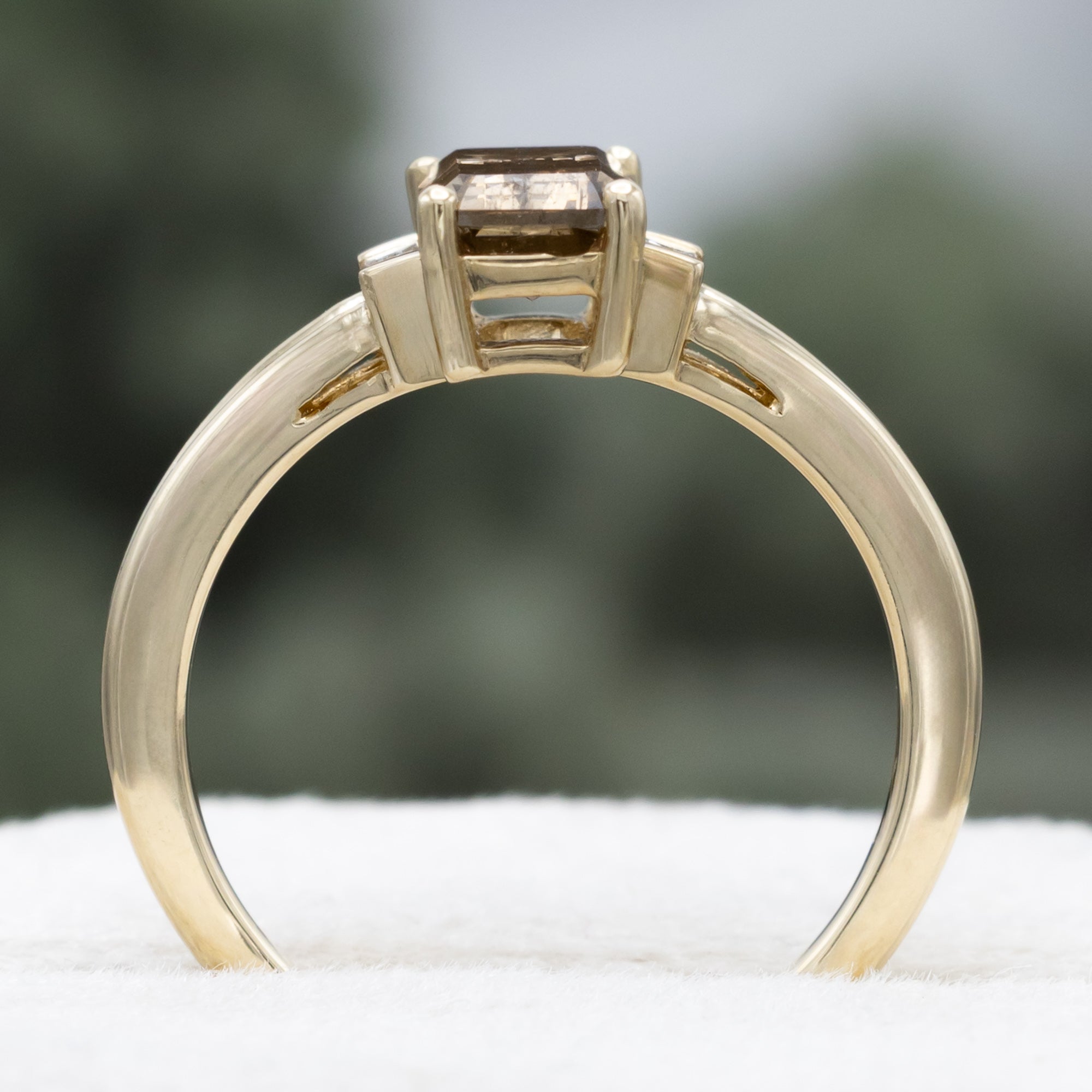 Gold ring with champagne diamond centerstone & diamond accent against a blurred green background