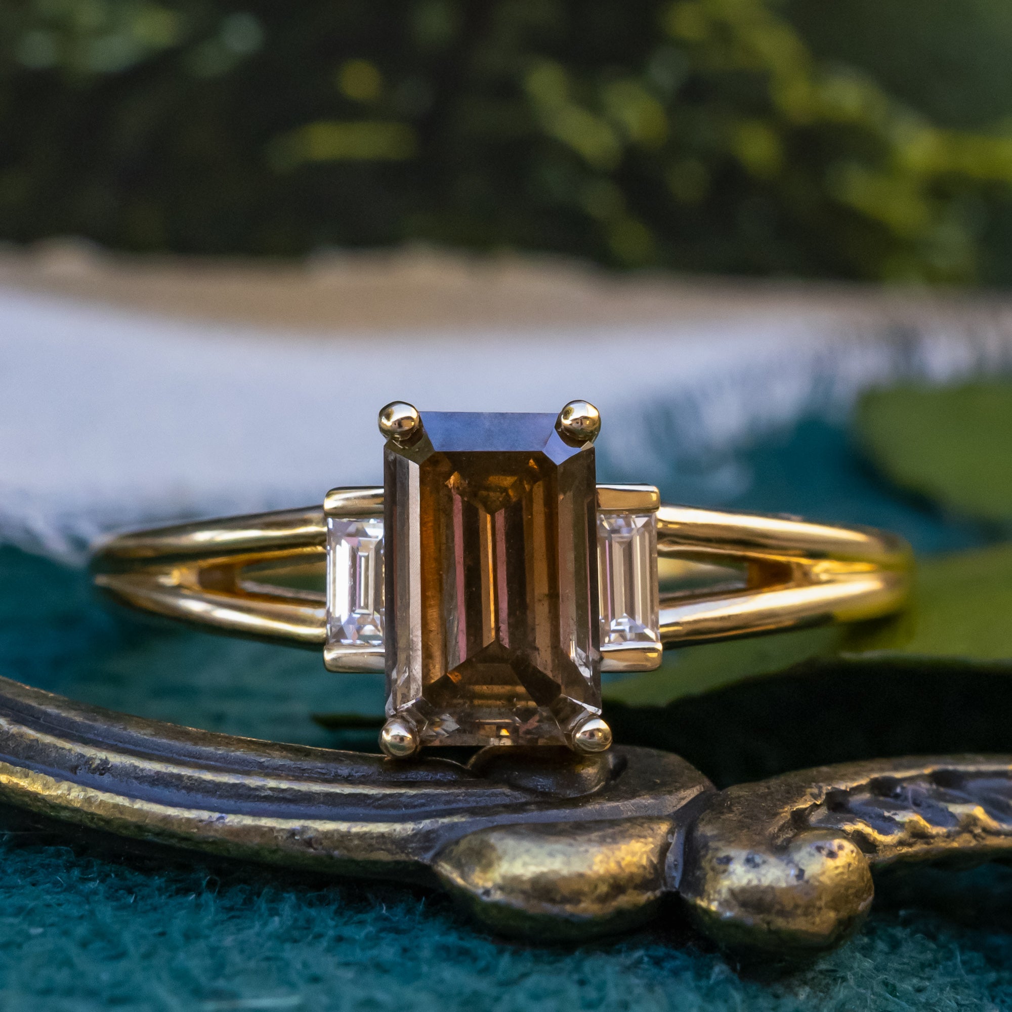 Gold ring with emerald cut champagne diamond on a decorative surface