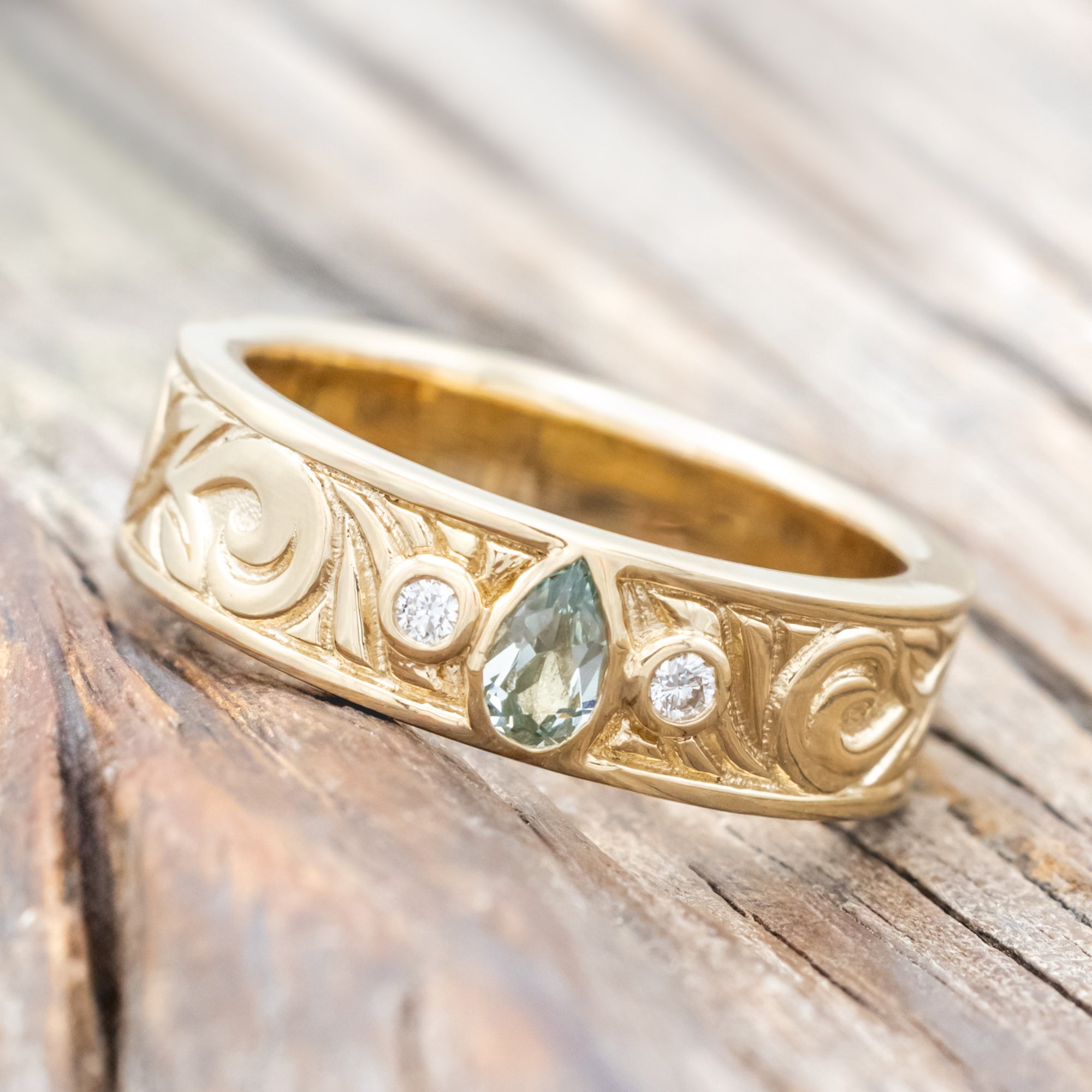 Yellow gold ring with lab sapphire and diamond accent on a wooden surface