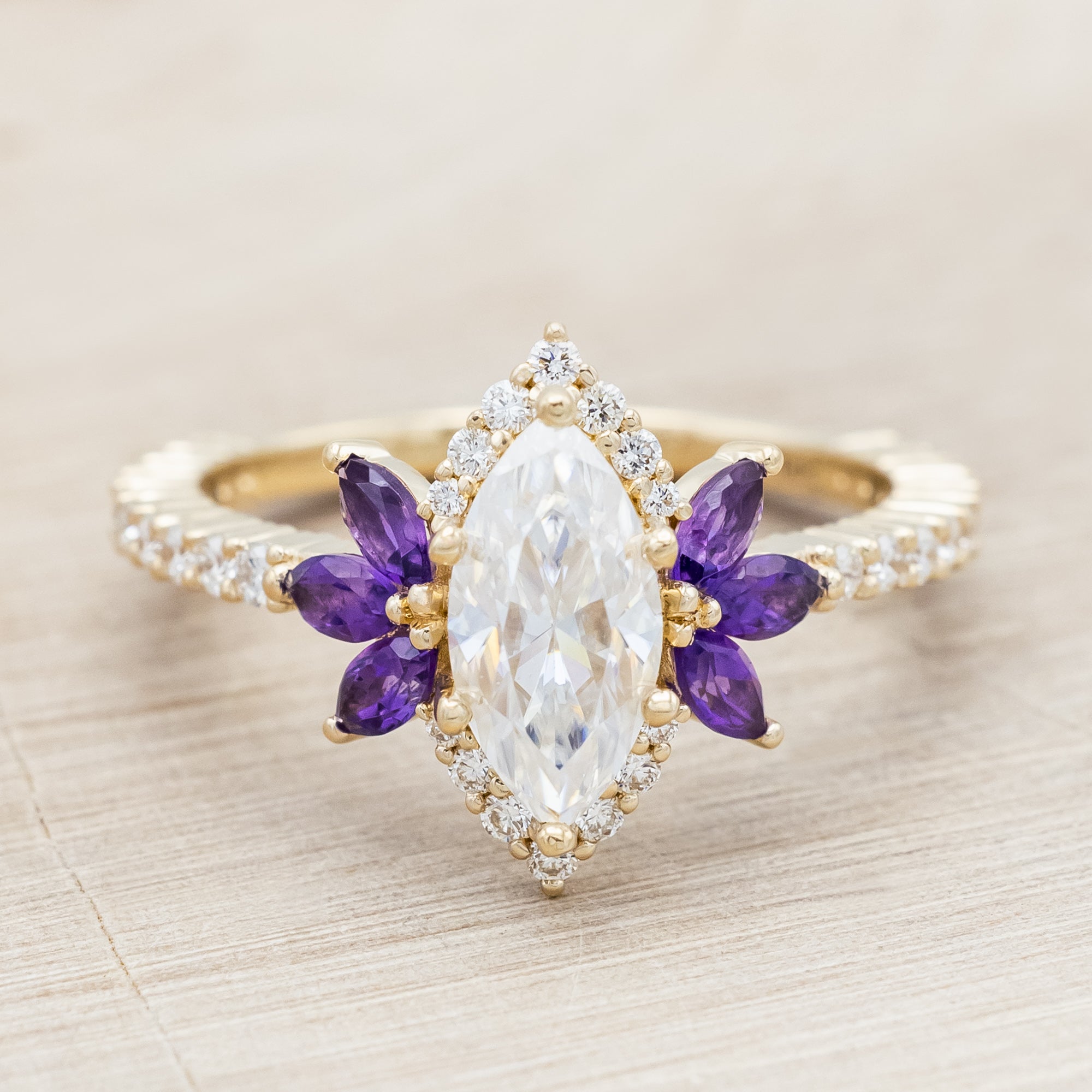 Yellow gold ring with a moissanite center stone and small purple amethyst accents on a beige background
