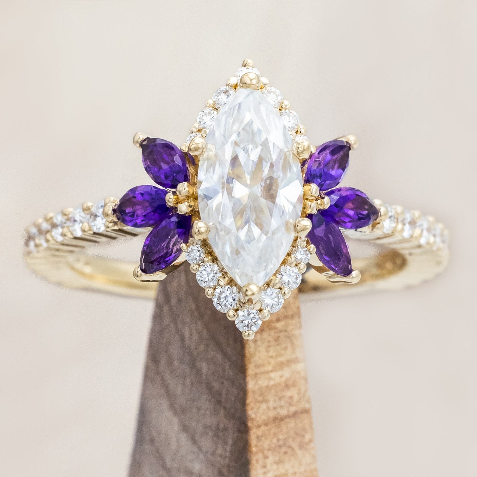 Yellow gold ring with a moissanite center stone and small purple amethyst accents on a beige background