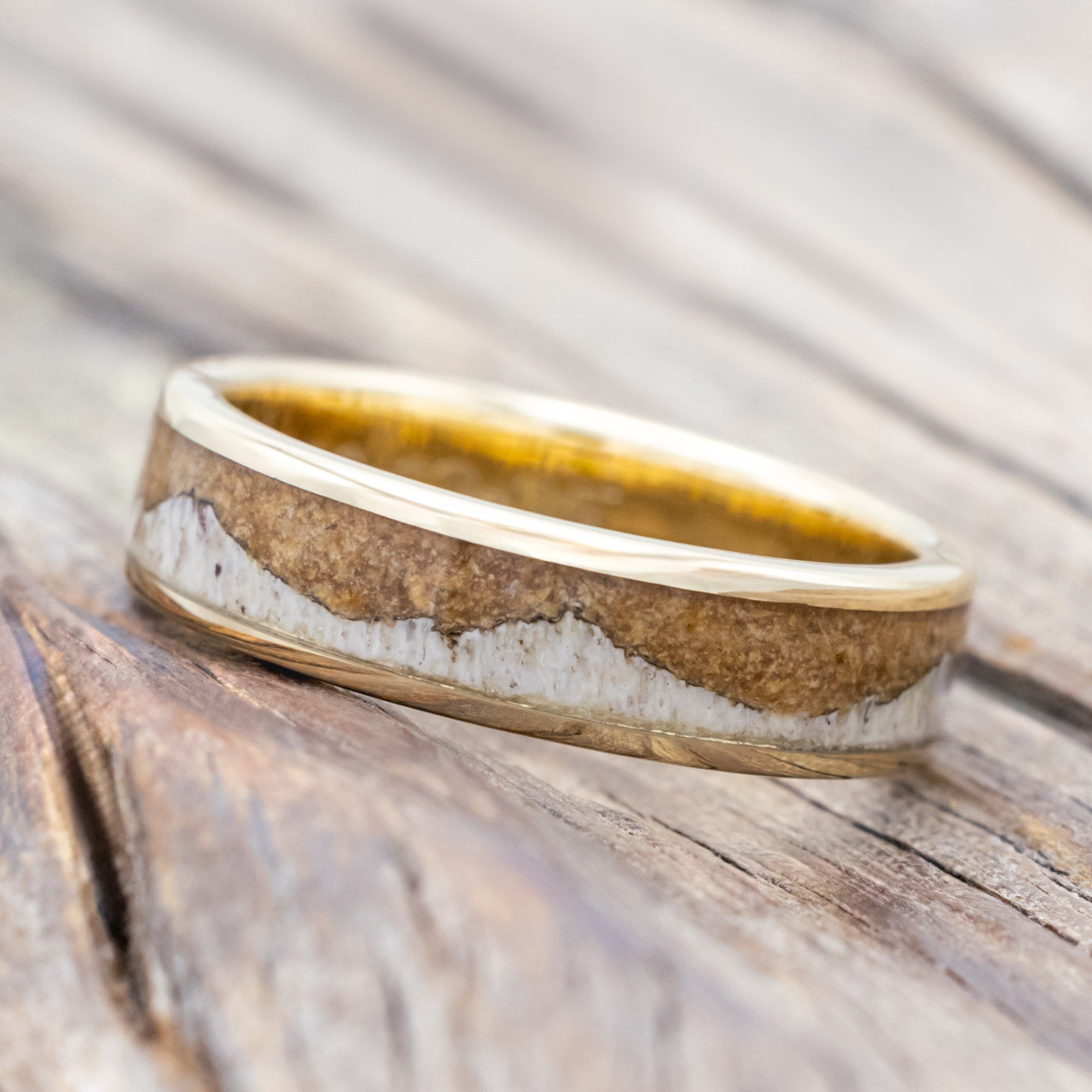 Yellow gold ring with powdered whiskey barrel and antler on a wooden surface.