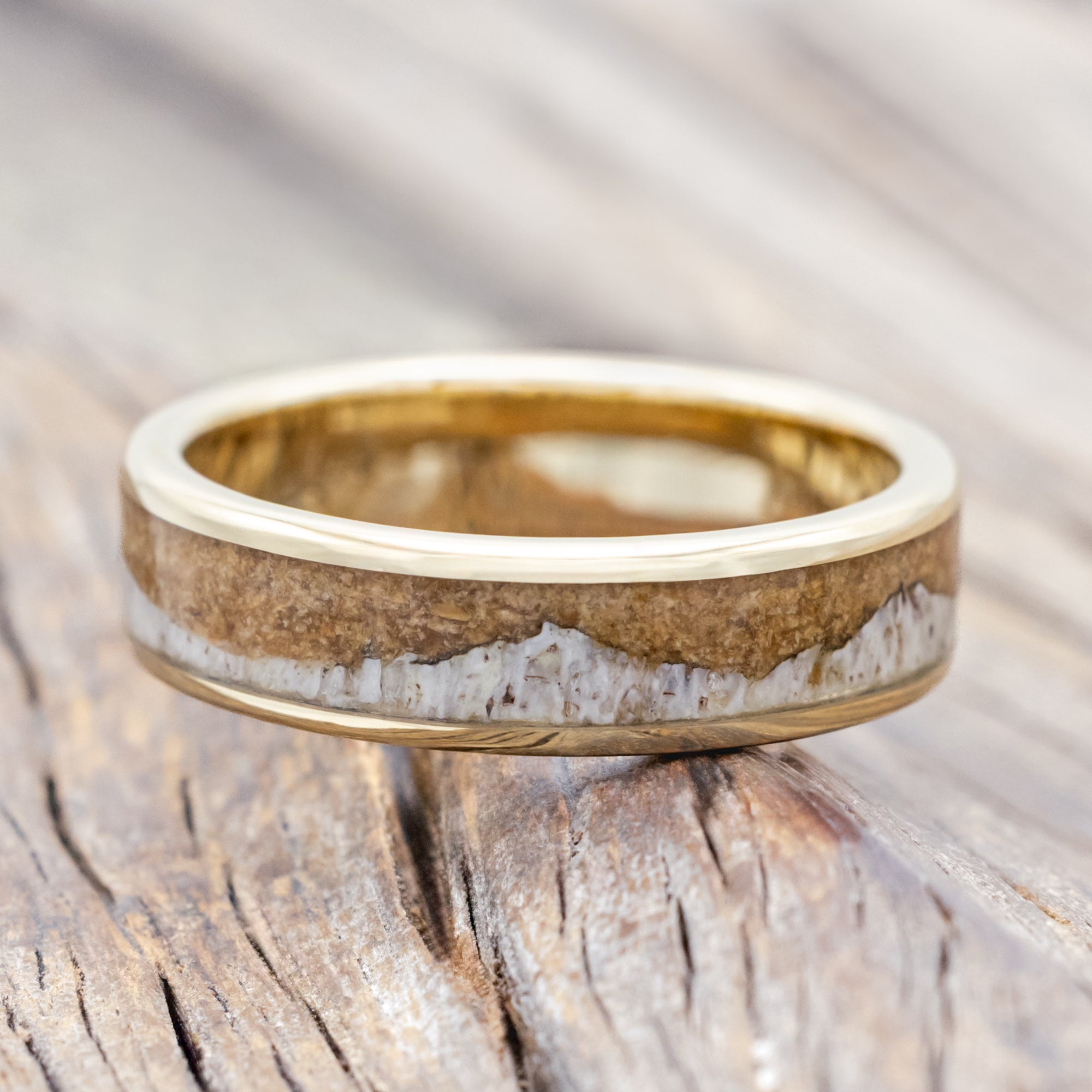 Yellow gold ring with powdered whiskey barrel and antler on a wooden surface.