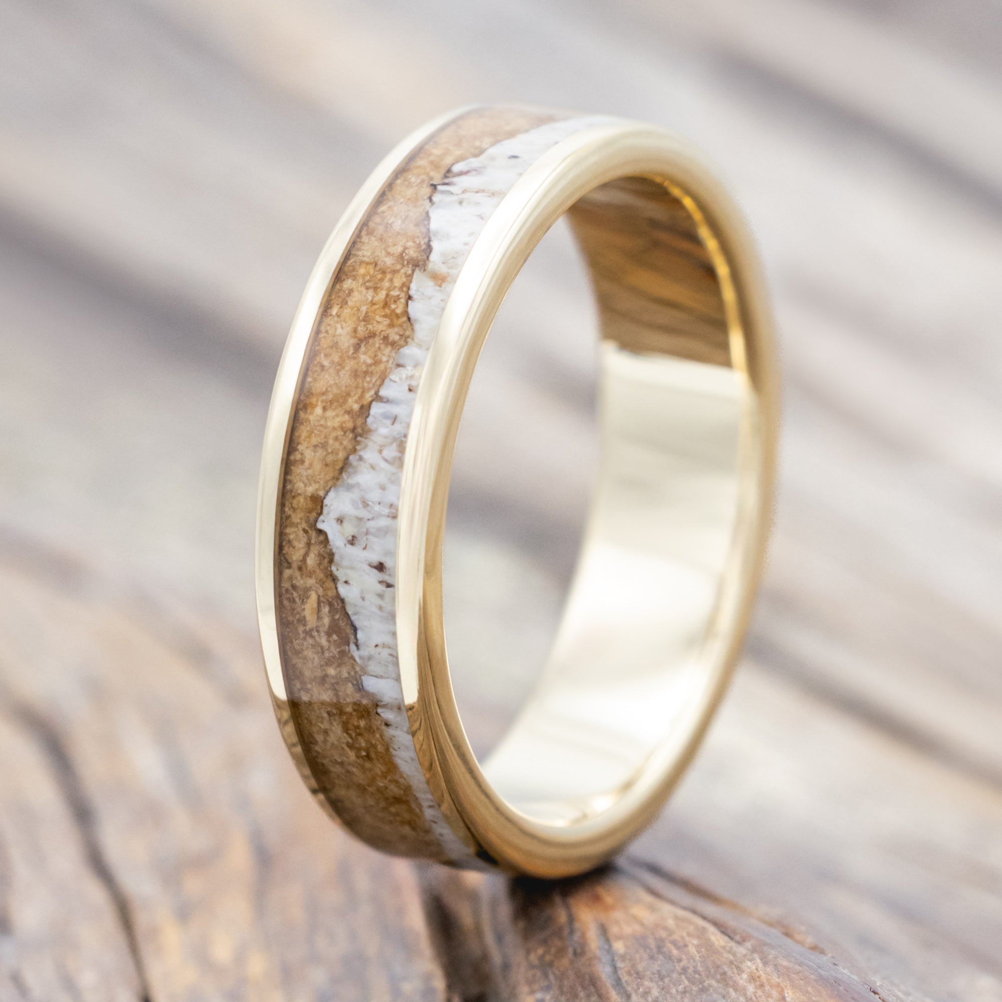 Yellow gold ring with powdered whiskey barrel and antler on a wooden surface.