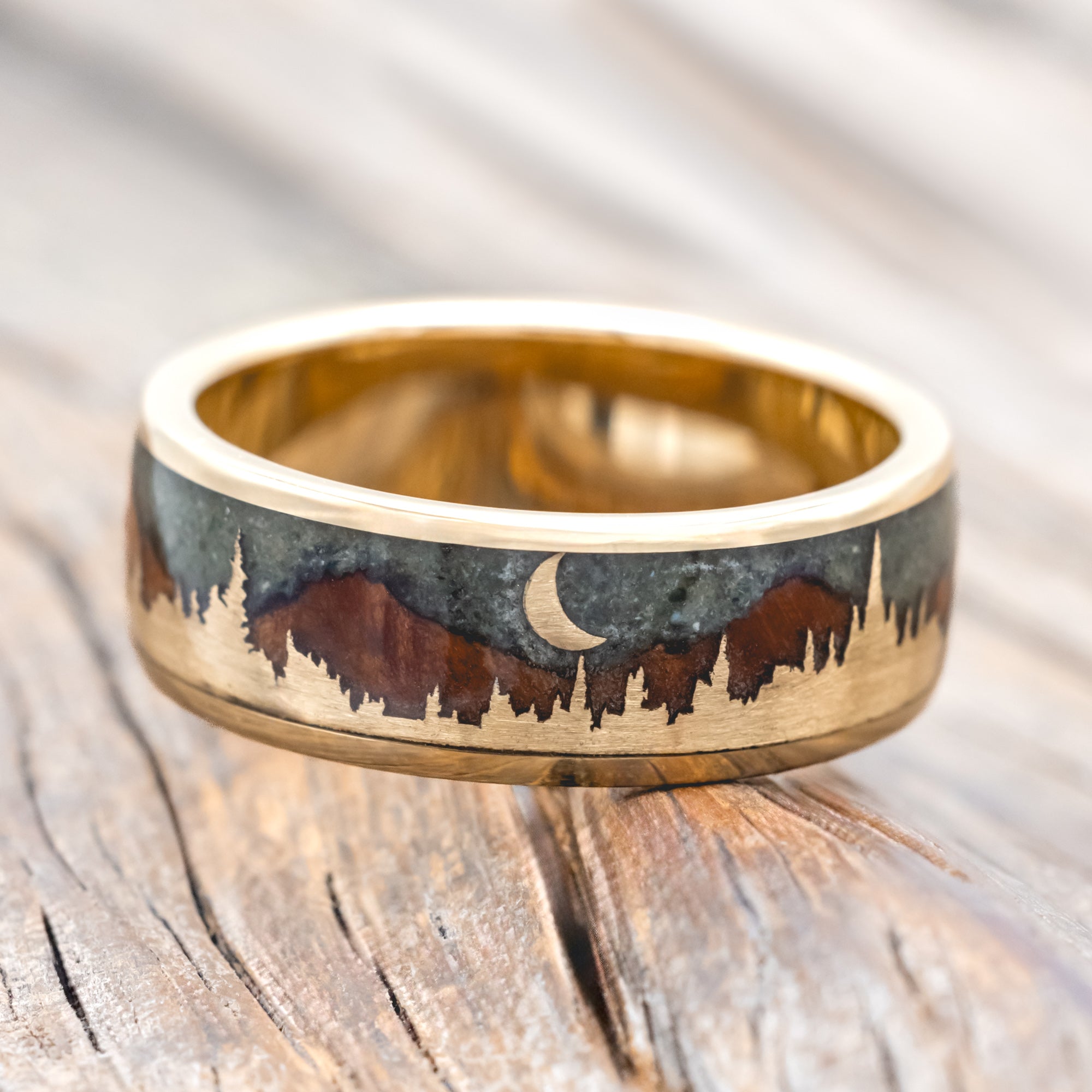 Ring with engraved design of mountains and a moon on a wooden surface
