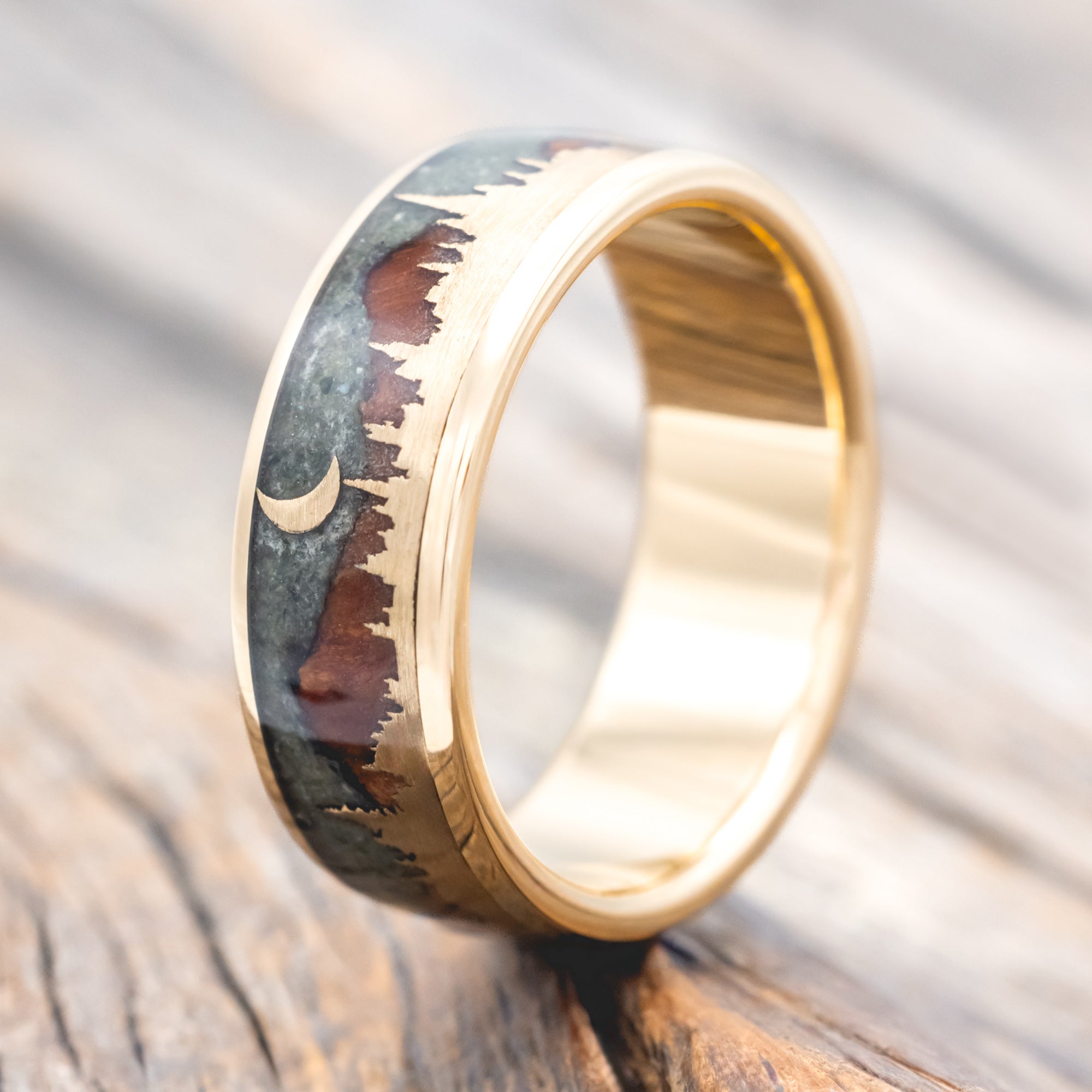 Ring with engraved design of mountains and a moon on a wooden surface