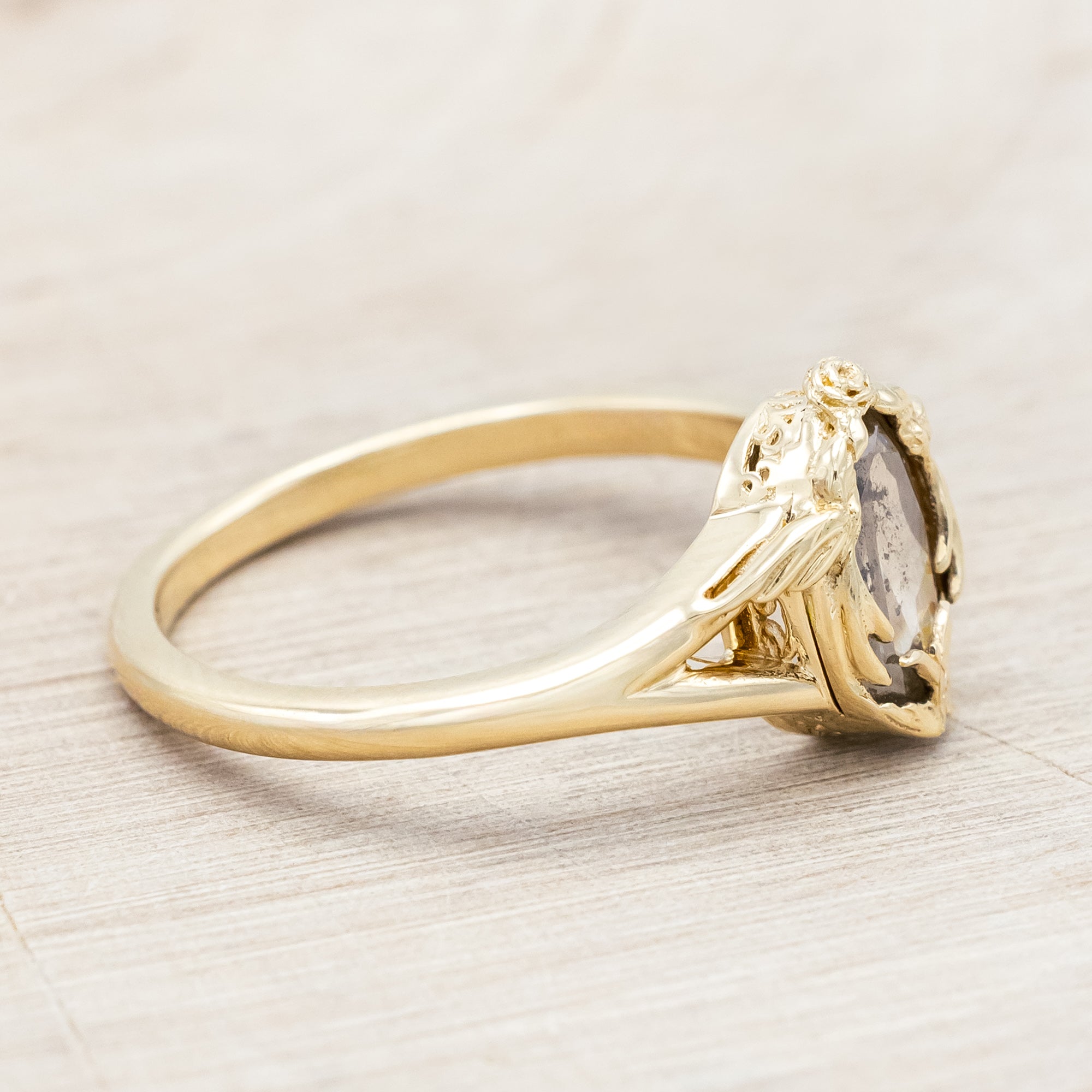 Gold ring with salt & pepper diamond with swallow filigree against beige background