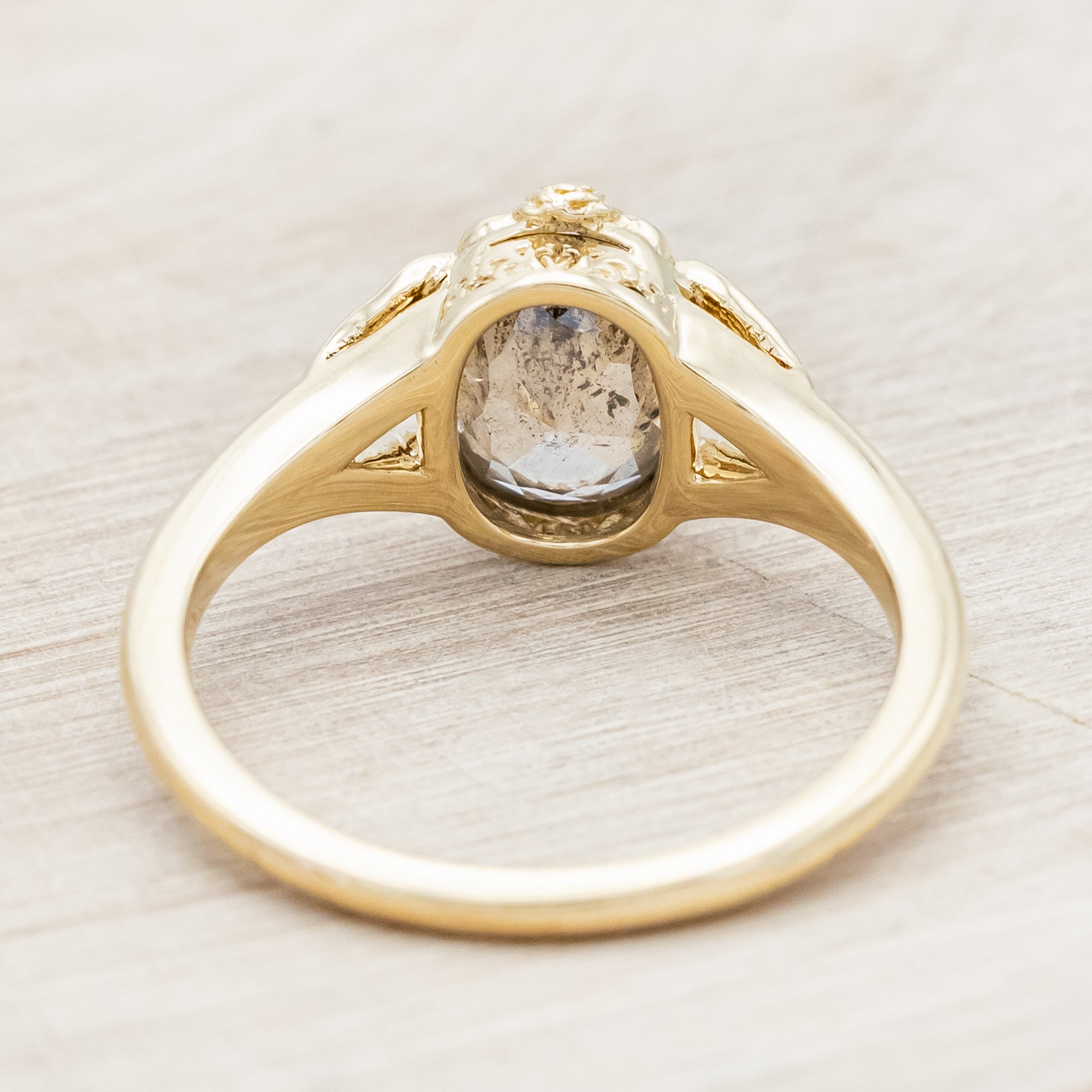 Gold ring with salt & pepper diamond with swallow filigree against beige background