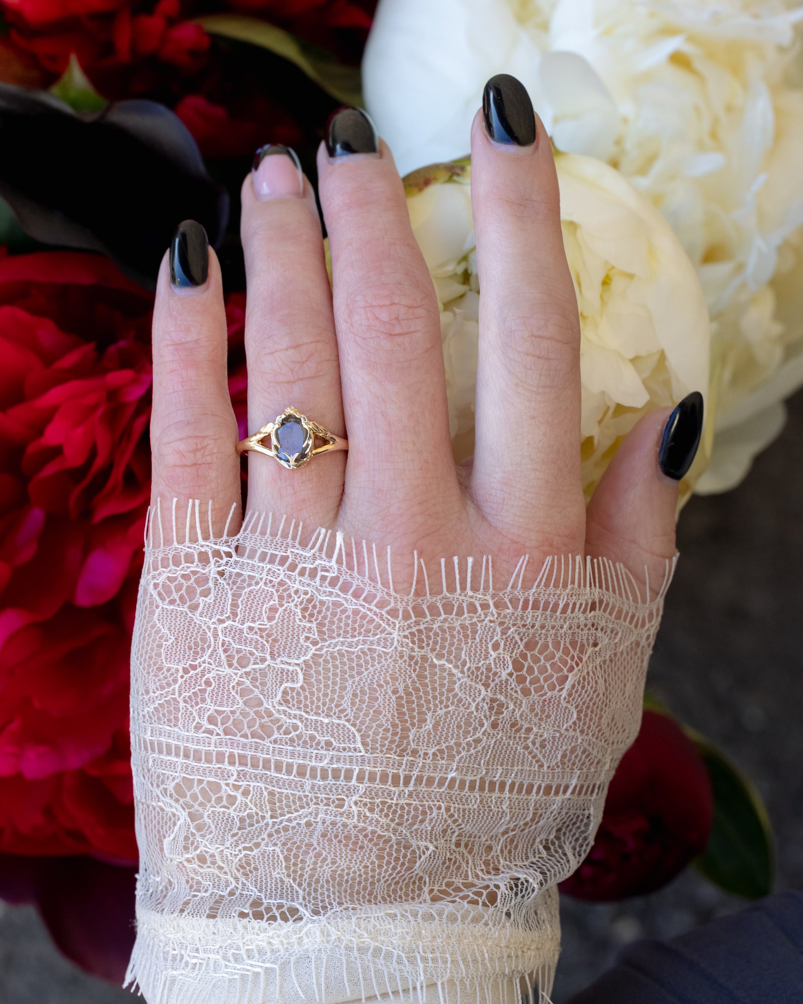 Hand wearing gold ring with salt & pepper diamond with swallow filigree against floral background