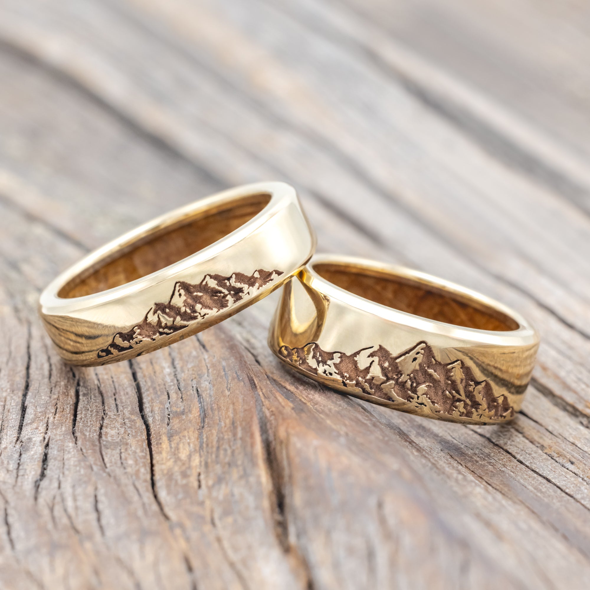 Two gold rings with mountain engraving on a wooden surface