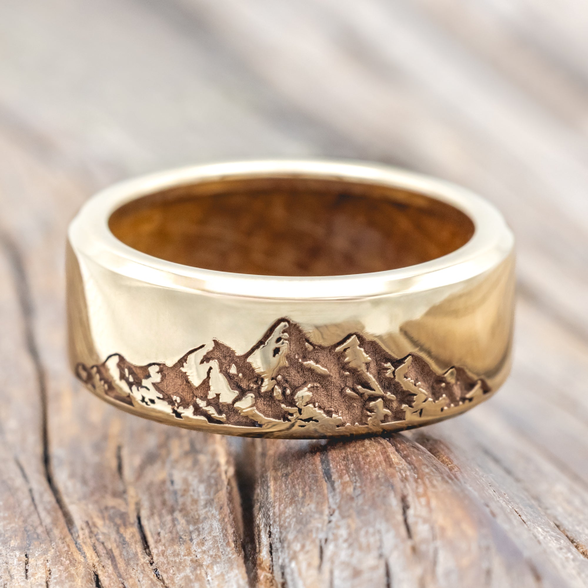 Gold ring with mountain engraving and whiskey barrel lining on a wooden surface