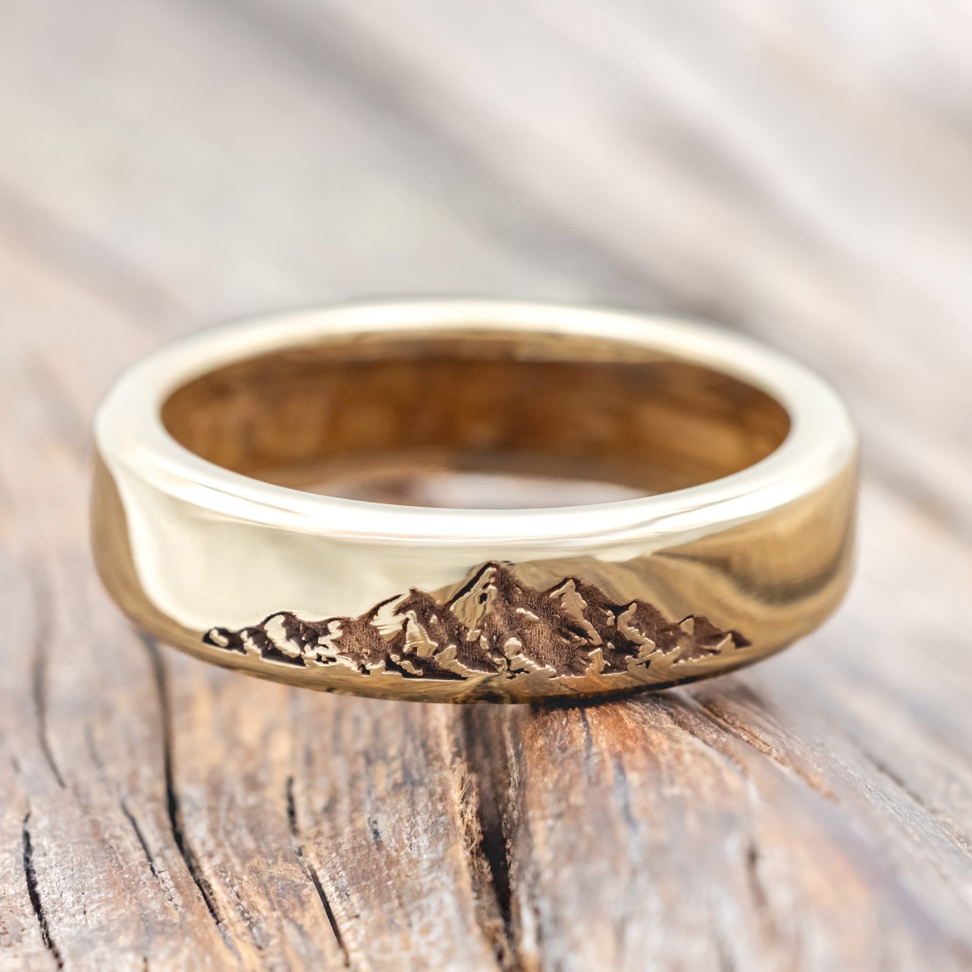 Gold ring with mountain engraving and whiskey barrel lining on a wooden surface