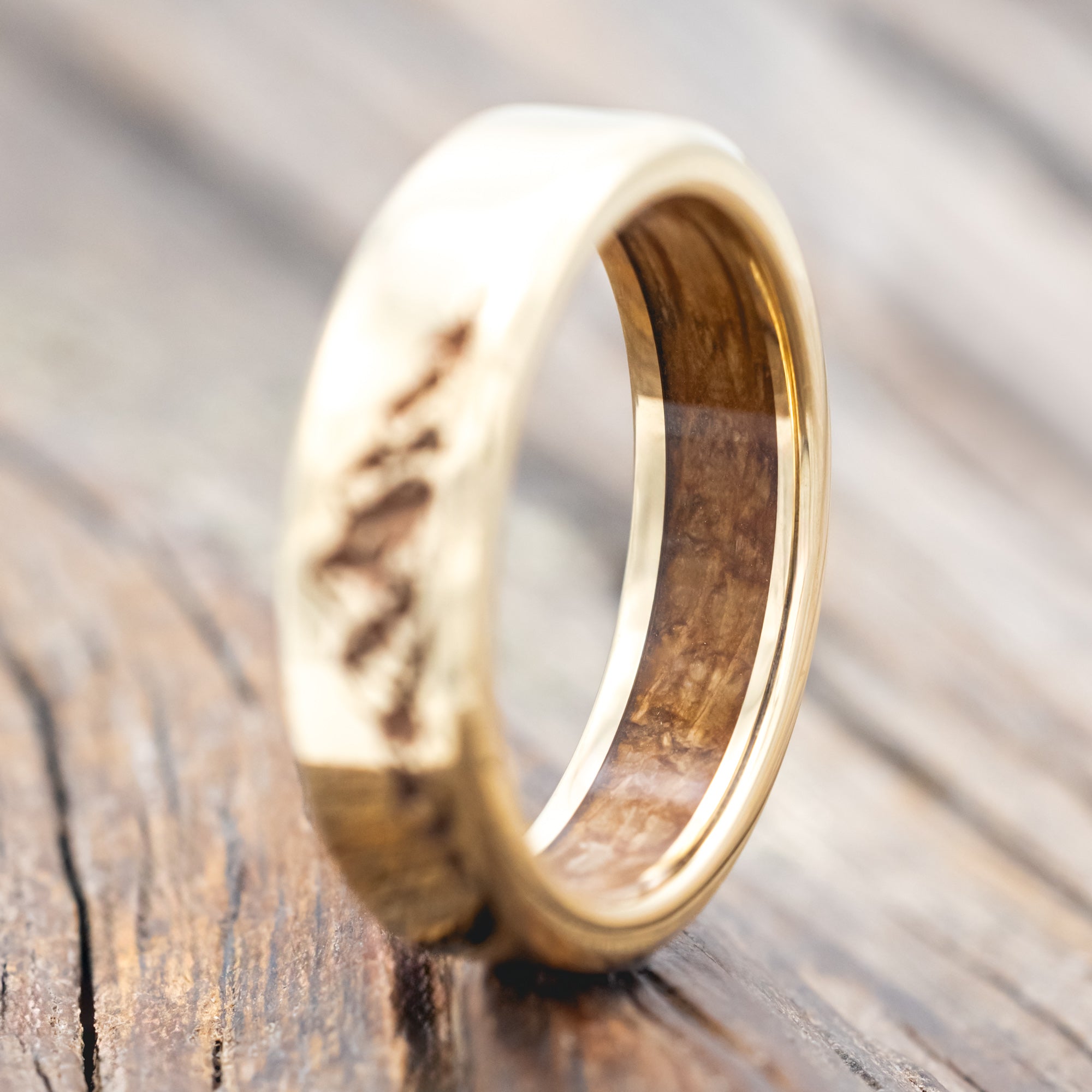 Gold ring with mountain engraving and whiskey barrel lining on a wooden surface