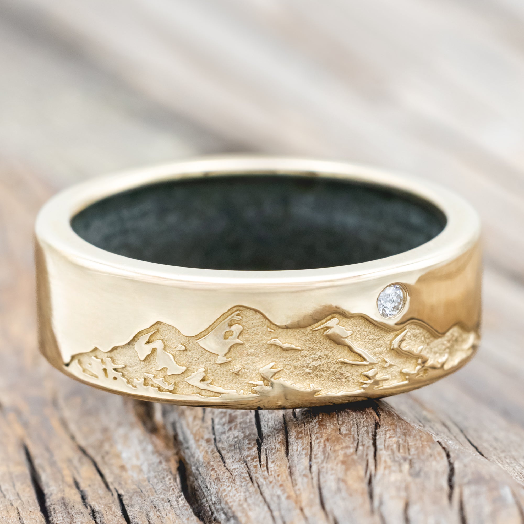 Gold ring with moss agate lining, diamond accent & mountain engraving on a wooden surface