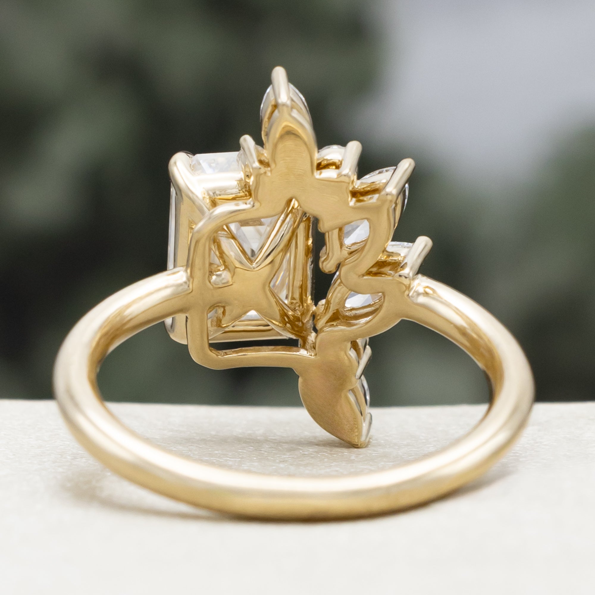 Gold ring with emerald-cut lab diamond and marquise diamond accents on a natural background