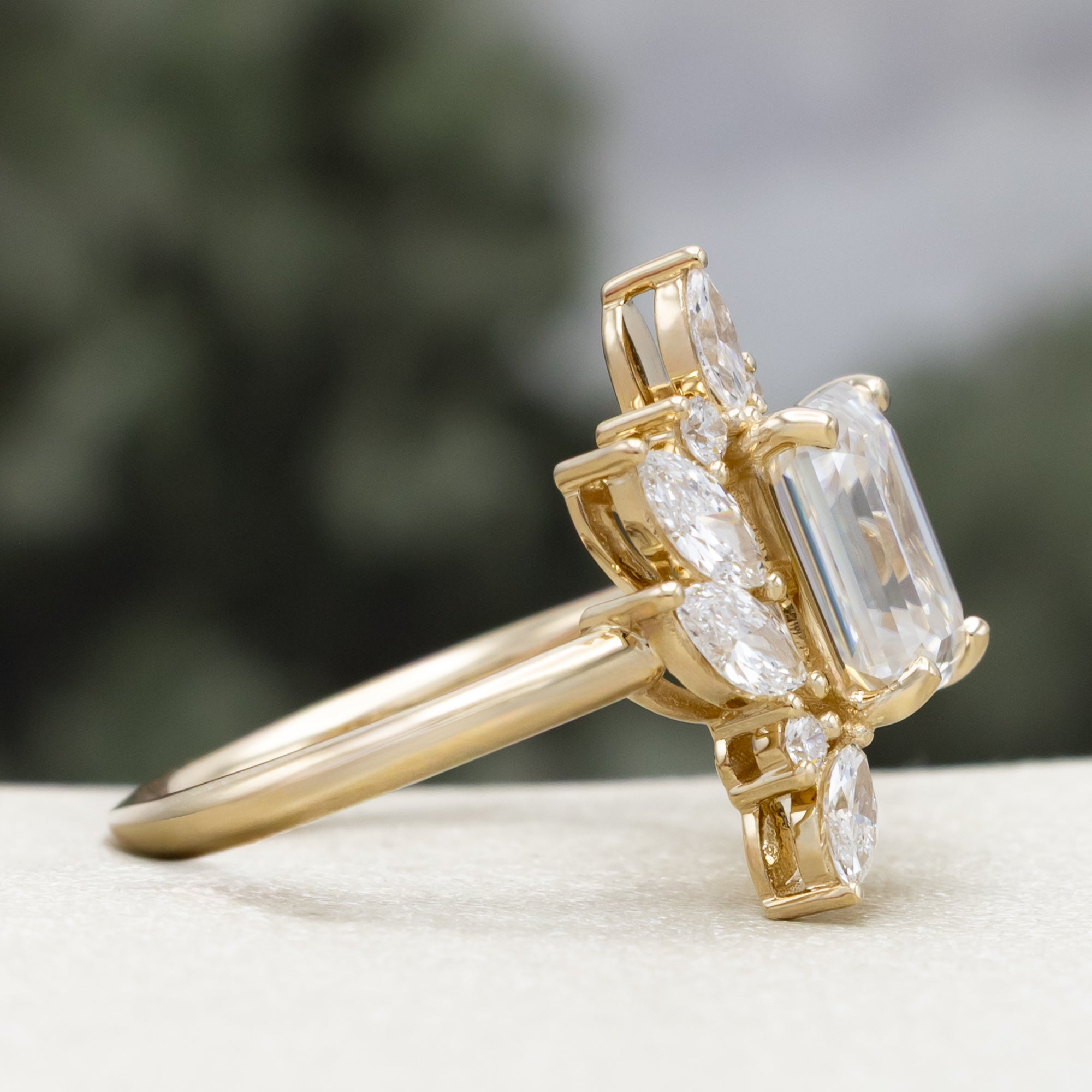 Gold ring with emerald-cut lab diamond and marquise diamond accents on a natural background