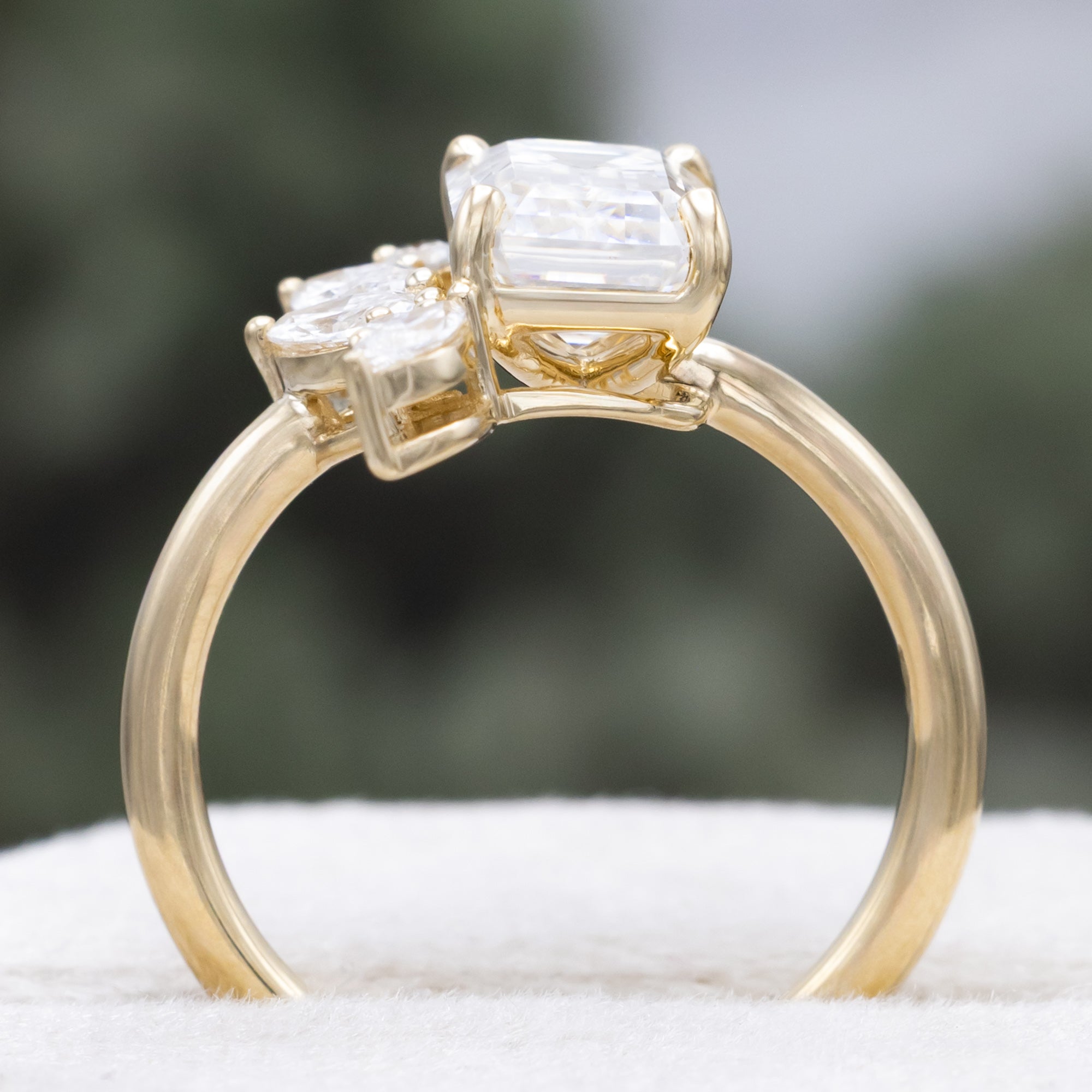Gold ring with emerald-cut lab diamond and marquise diamond accents on a natural background