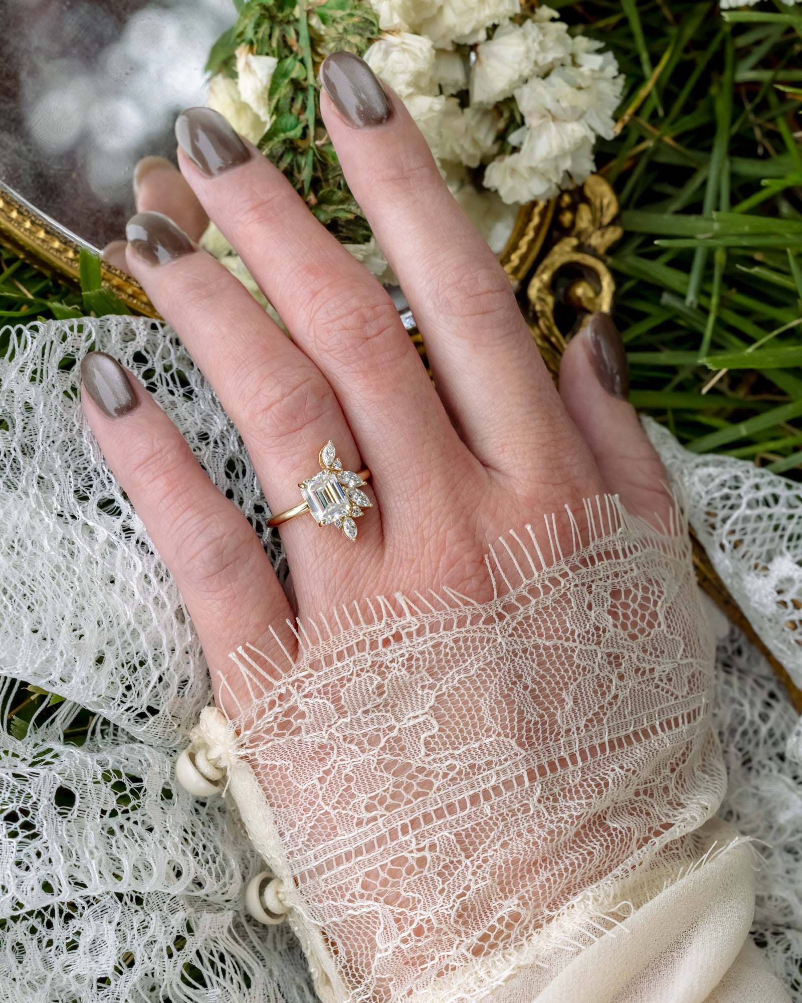 Gold ring with a lab diamond center stone and diamond accents on a hand against a textured background