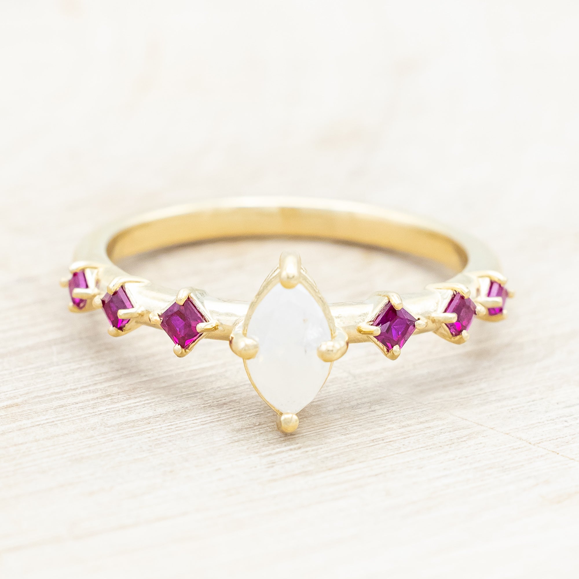 Gold ring with a central icy salt & pepper diamond with ruby accents on a beige background