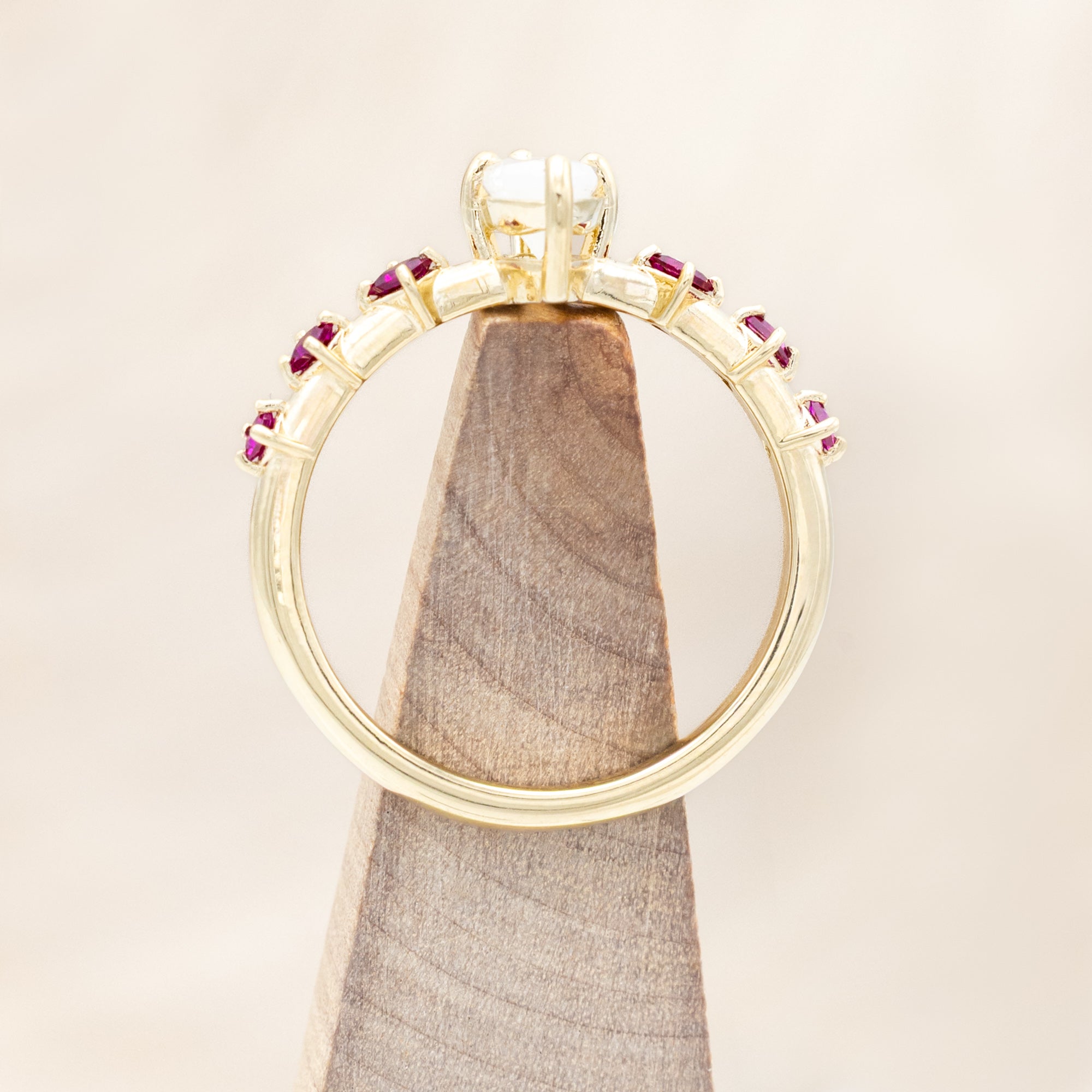 Gold ring with a central icy salt & pepper diamond with ruby accents on a beige background