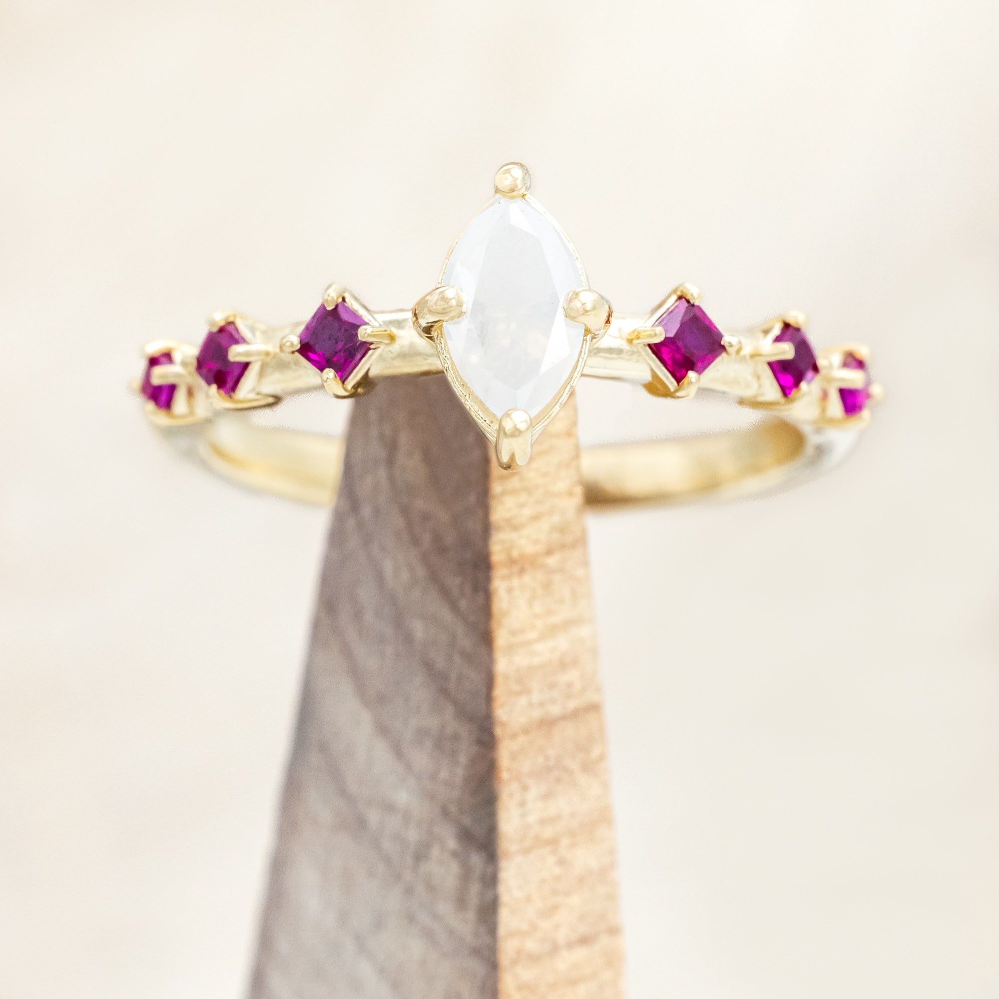 Gold ring with a central icy salt & pepper diamond with ruby accents on a beige background