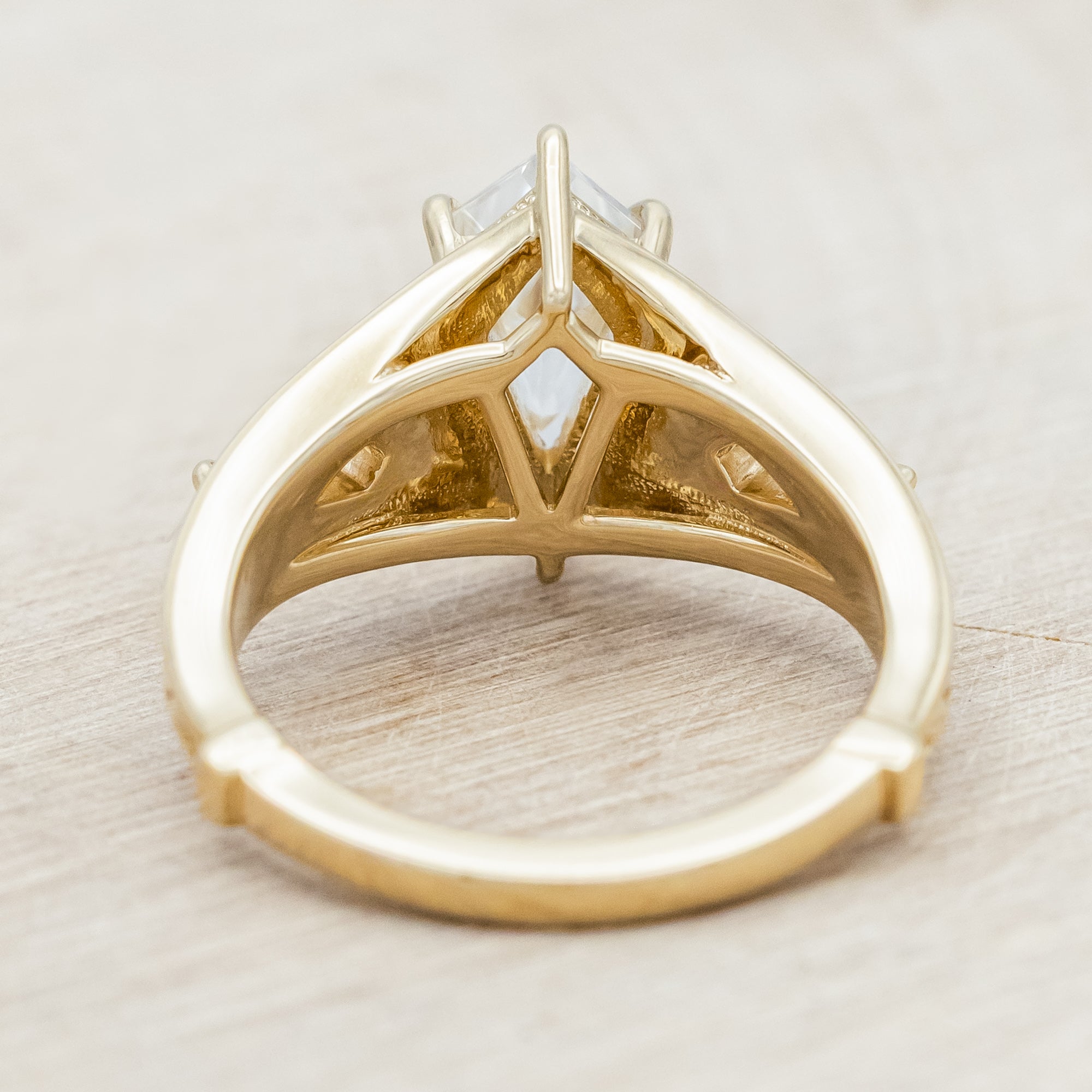 14K yellow gold ring with kite cut Moissanite and two smaller Moissanite accents on a light wooden background
