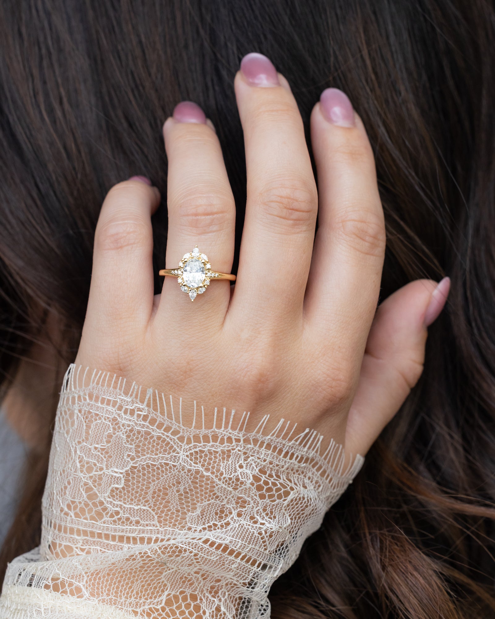 Hand wearing a gold ring with a lab diamond, held against a blurred background