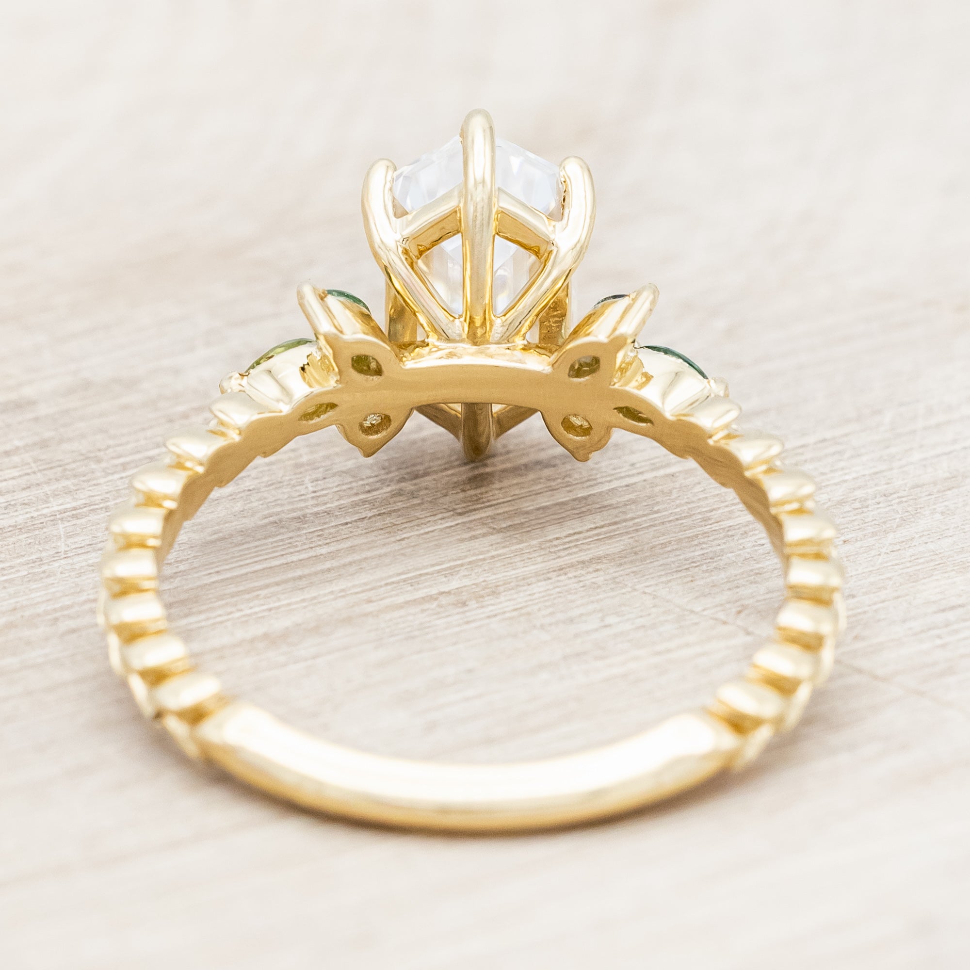 Gold ring with hexagon-cut diamond and green gemstone accents on a beige background