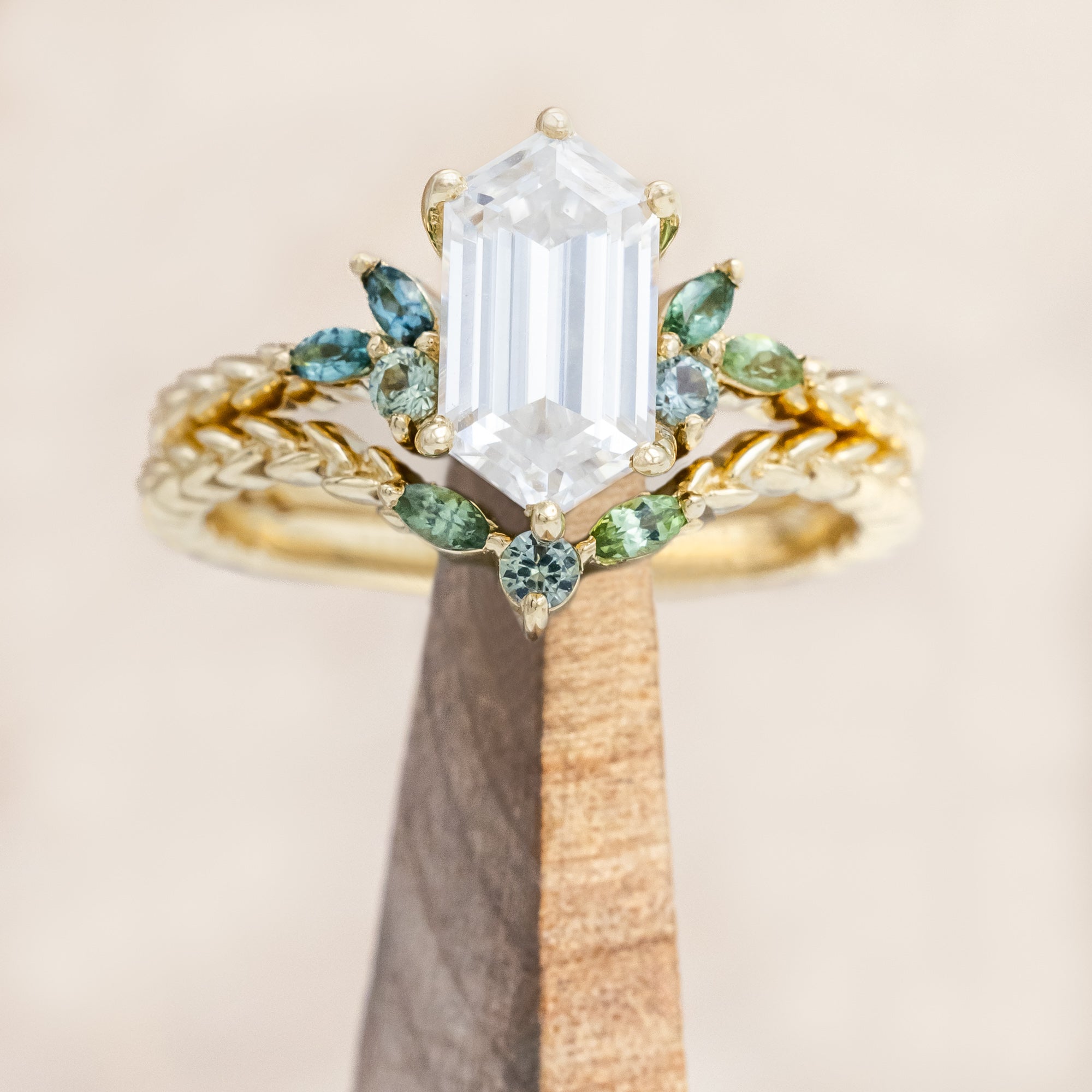 Gold ring with hexagon-cut diamond and green gemstone accents on a beige background