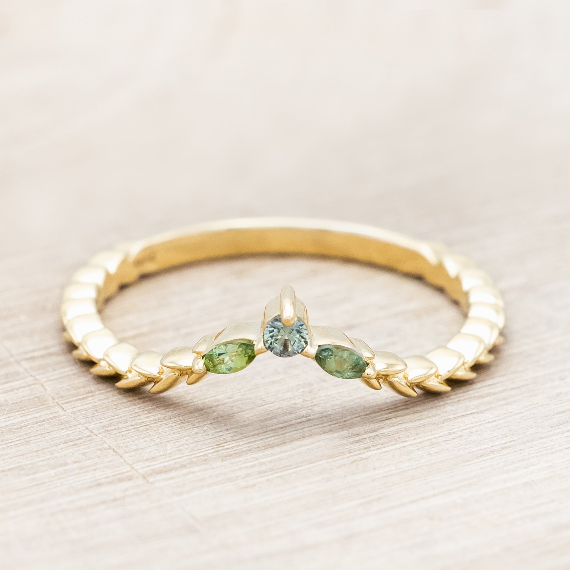 Gold ring with sapphire and tourmaline accents against a beige background