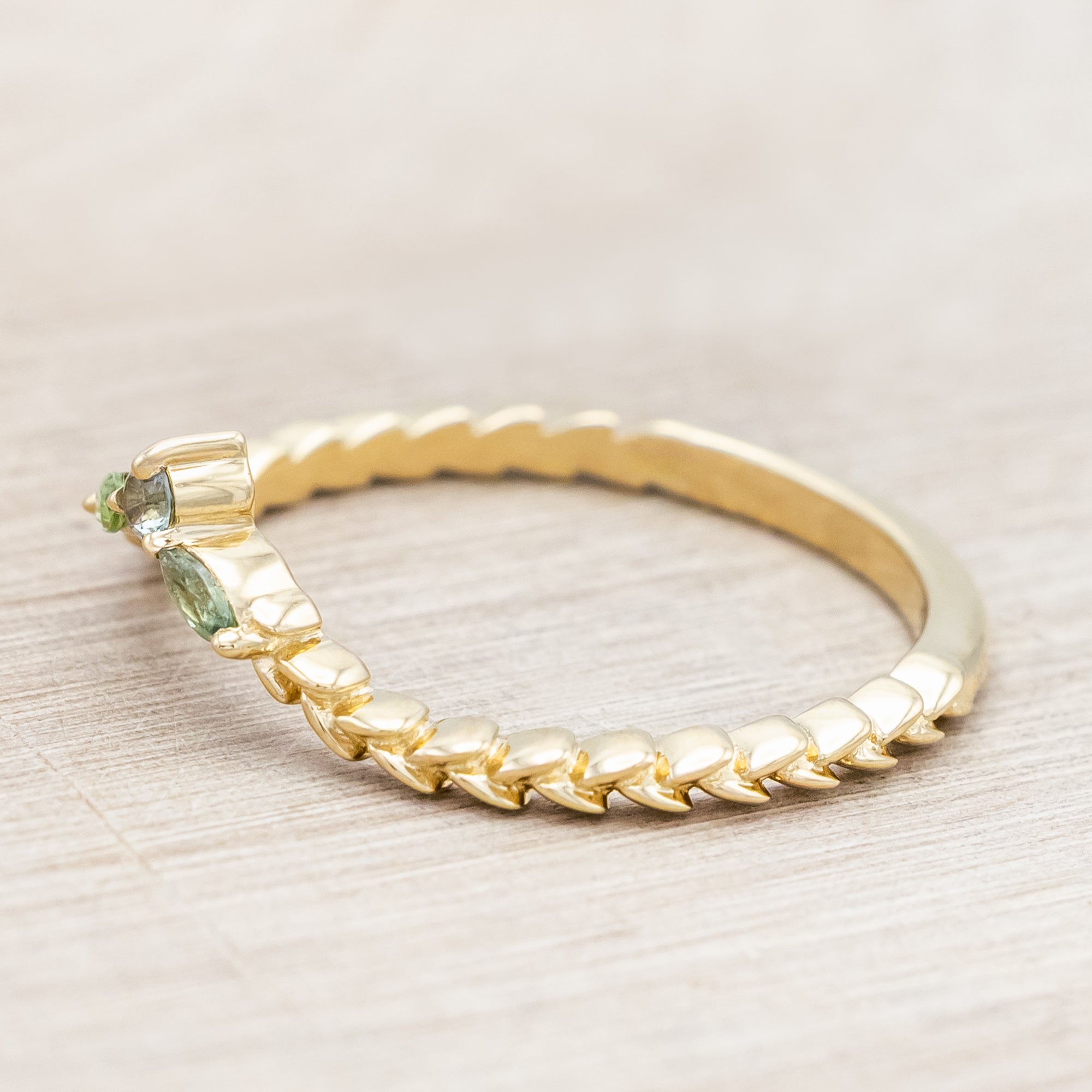 Gold ring with sapphire and tourmaline accents against a beige background