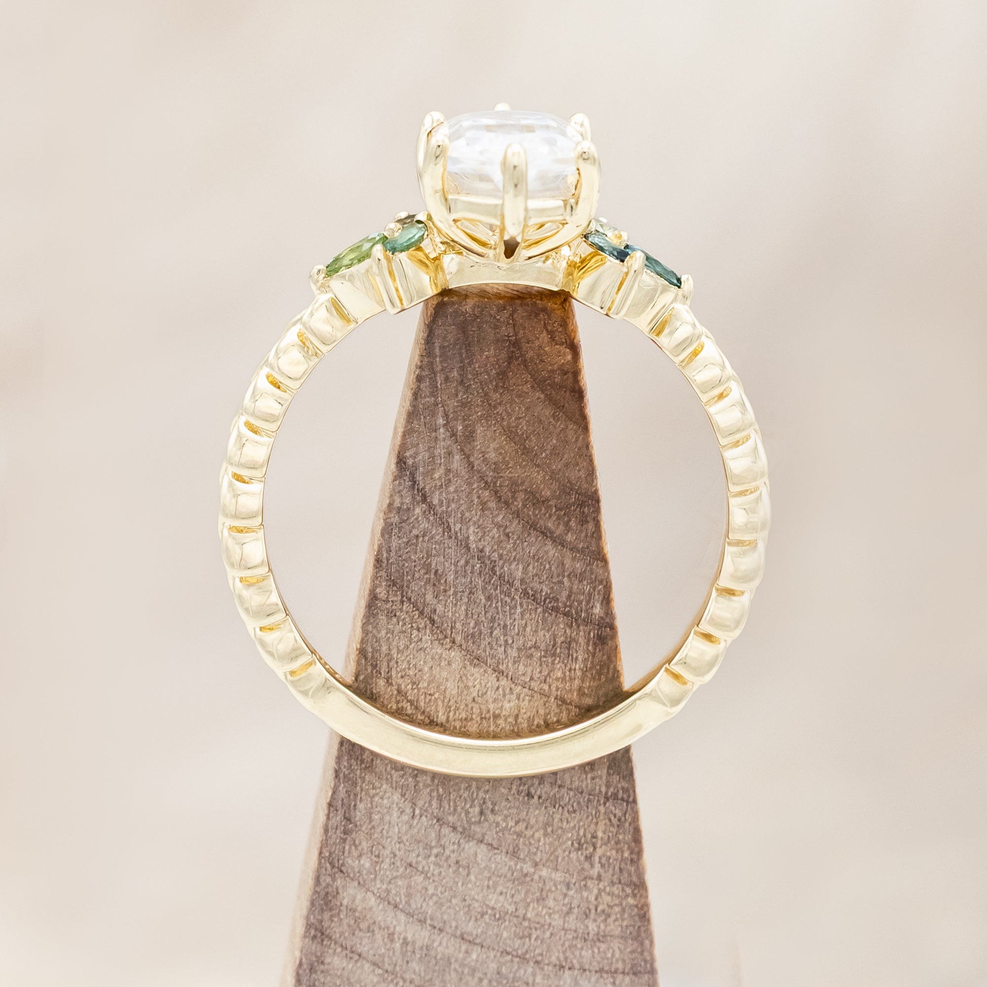 Gold ring with hexagon-cut diamond and green gemstone accents on a beige background