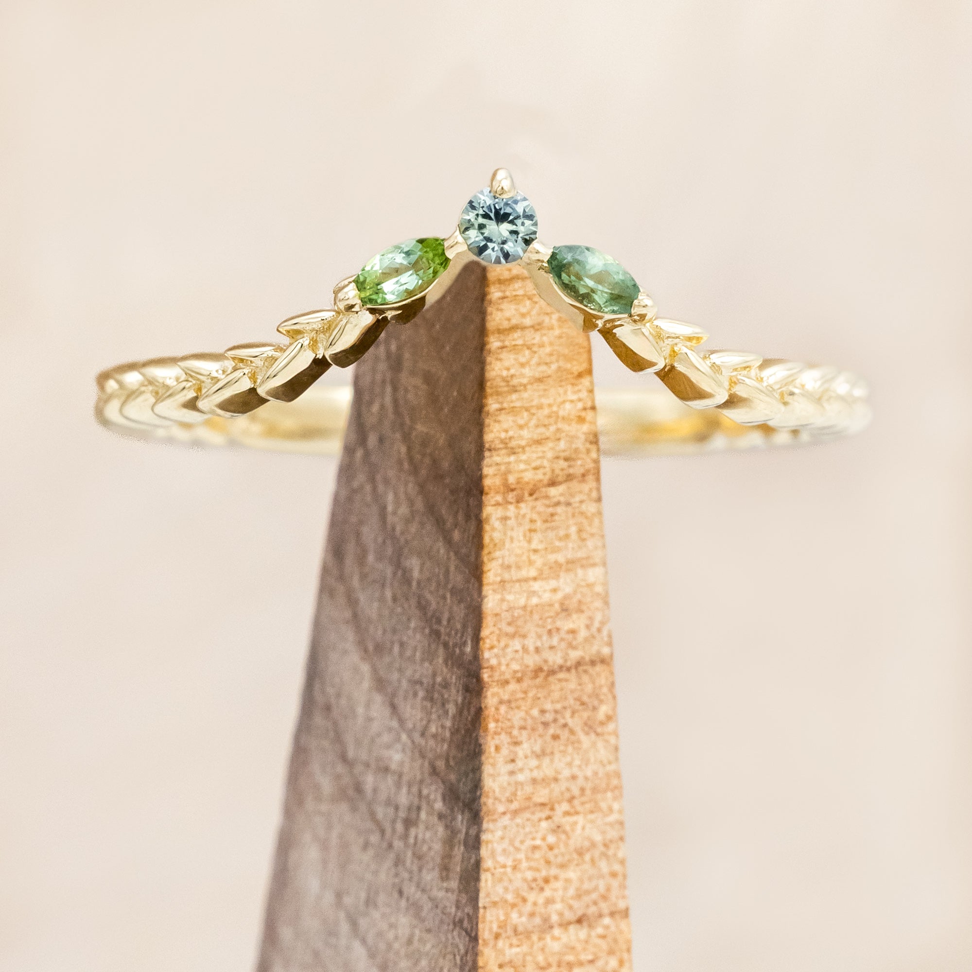 Gold ring with sapphire and tourmaline accents on a wooden stand against a beige background