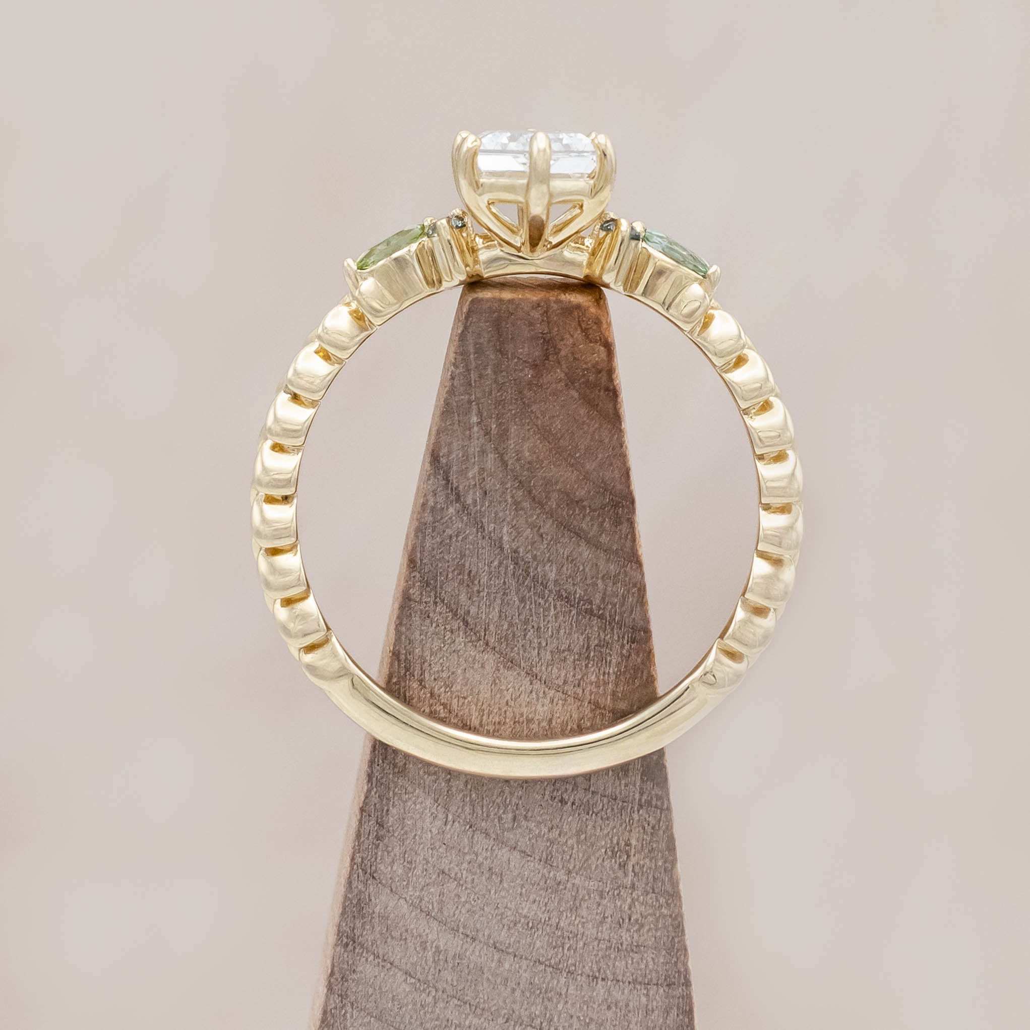 14K gold ring with diamond center stone featuring green sapphire and tourmaline accents on a light wooden background