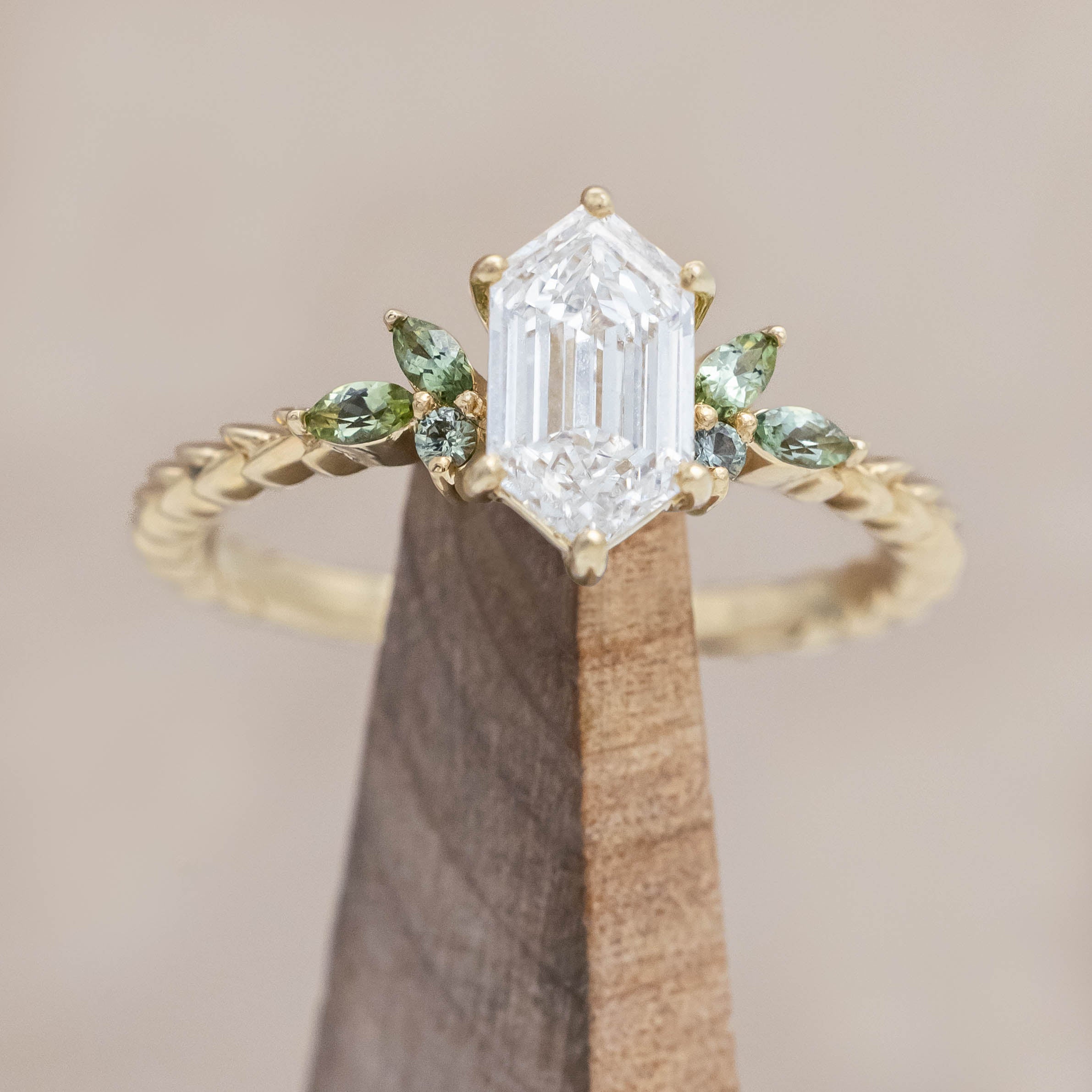 14K gold ring with diamond center stone featuring green sapphire and tourmaline accents on a wooden stand against a beige background