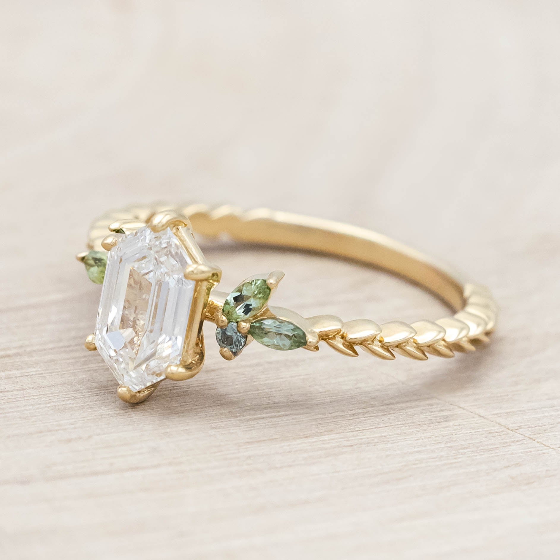 14K gold ring with diamond center stone featuring green sapphire and tourmaline accents on a light wooden background