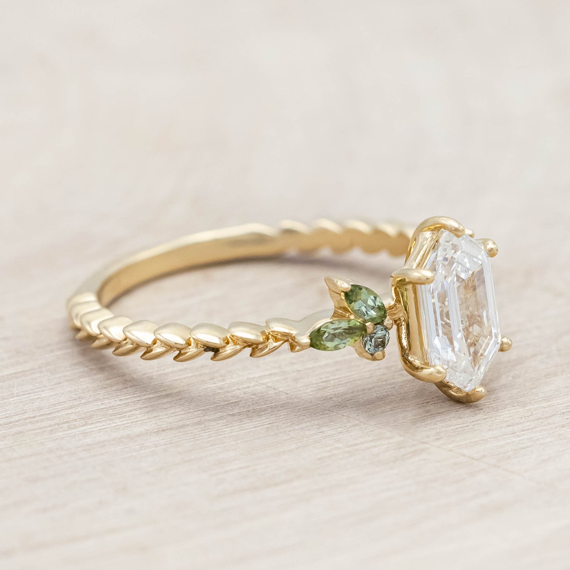 14K gold ring with diamond center stone featuring green sapphire and tourmaline accents on a light wooden background