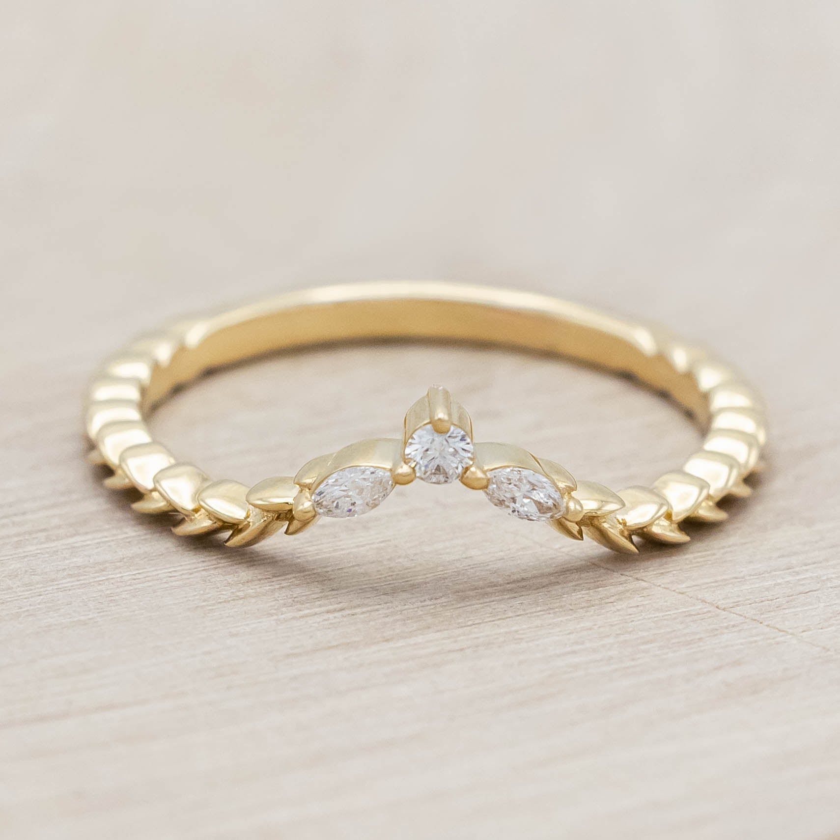 14K gold ring with three diamonds on a wooden stand against a beige background
